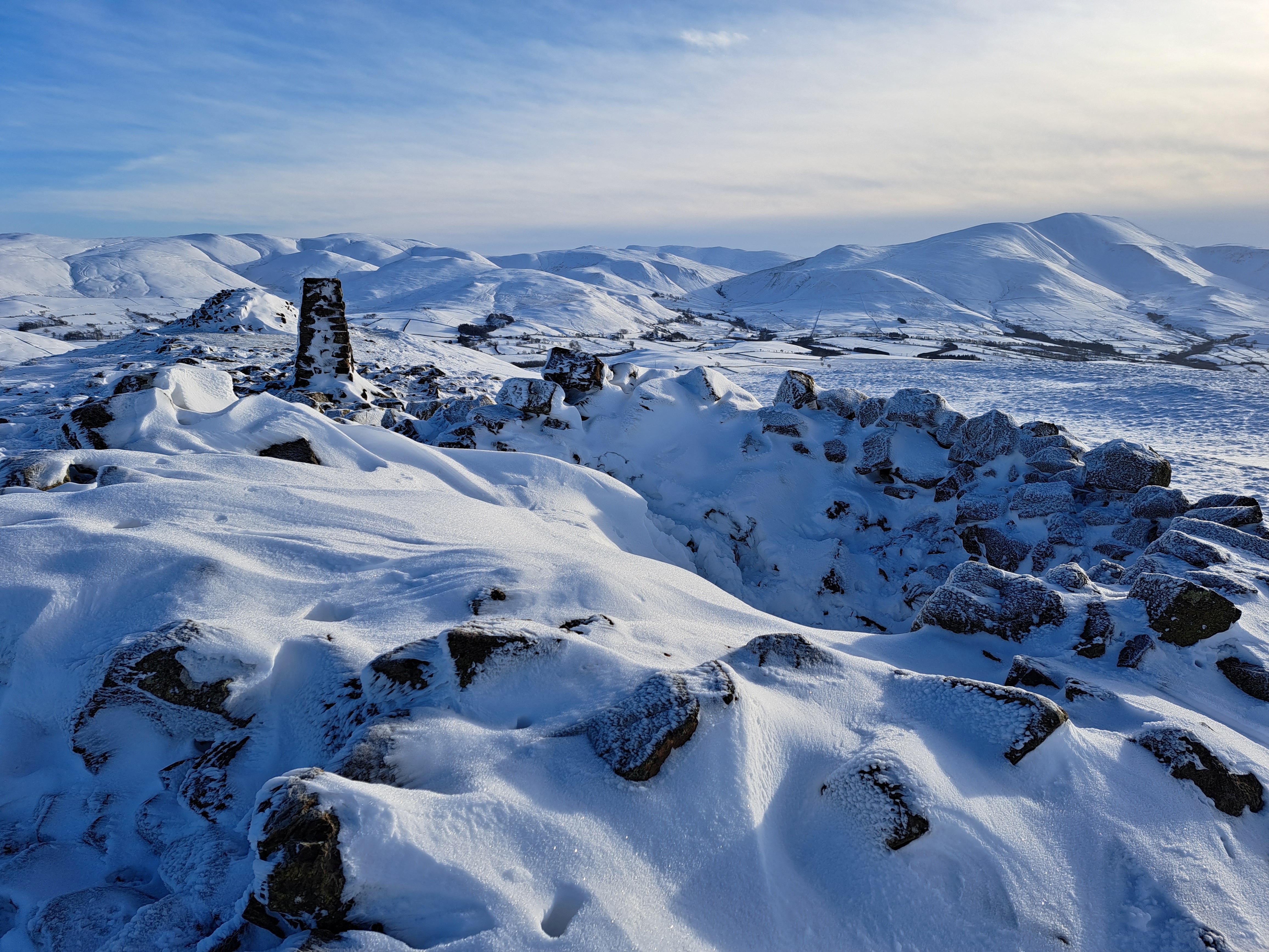 A snow covered cairn is seen at the summit of Binsey Fell