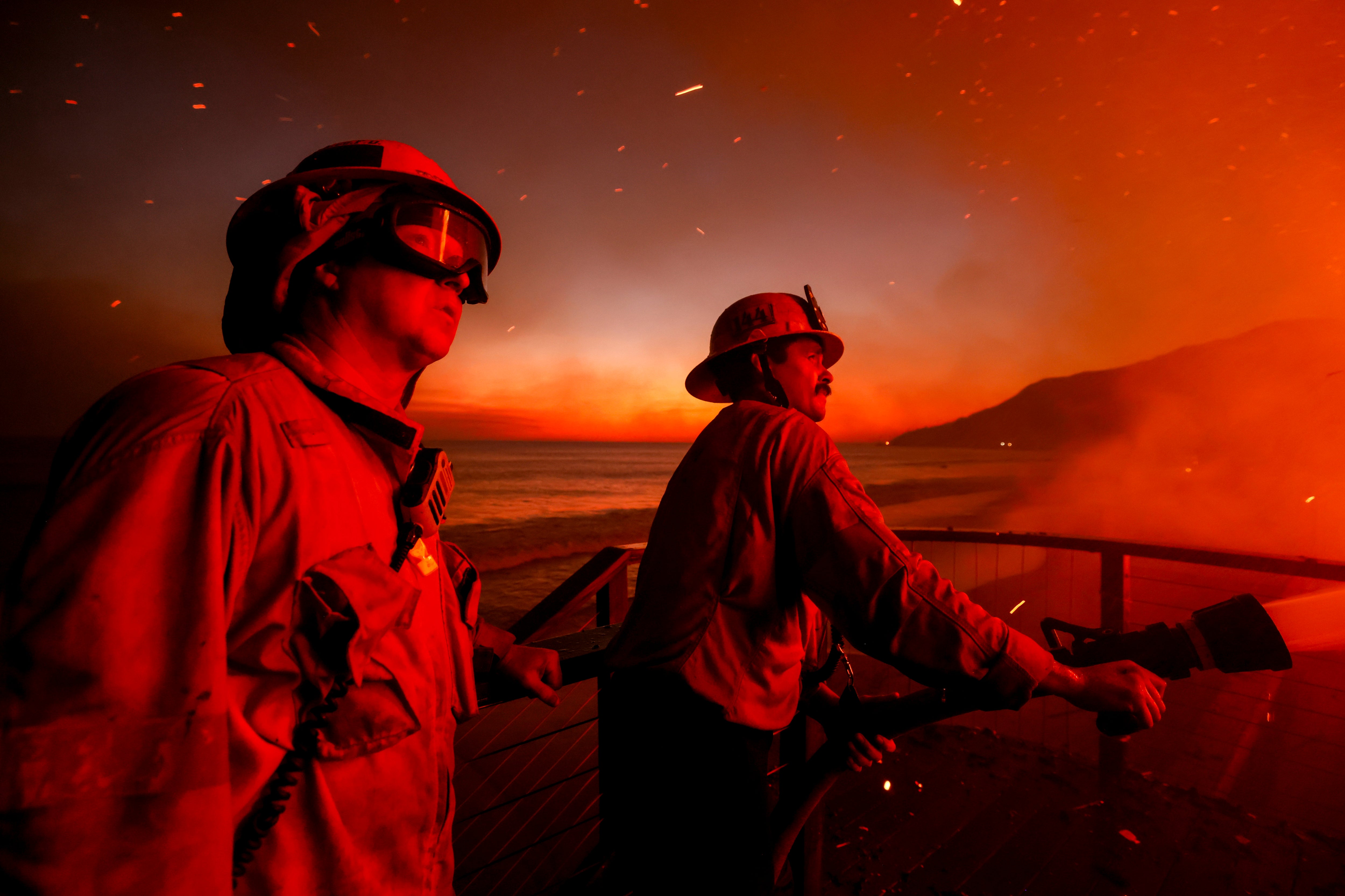 Firefighters work from a deck as the Palisades Fire burns a beachfront property on Wednesday in Malibu, California. The winds died down slightly overnight