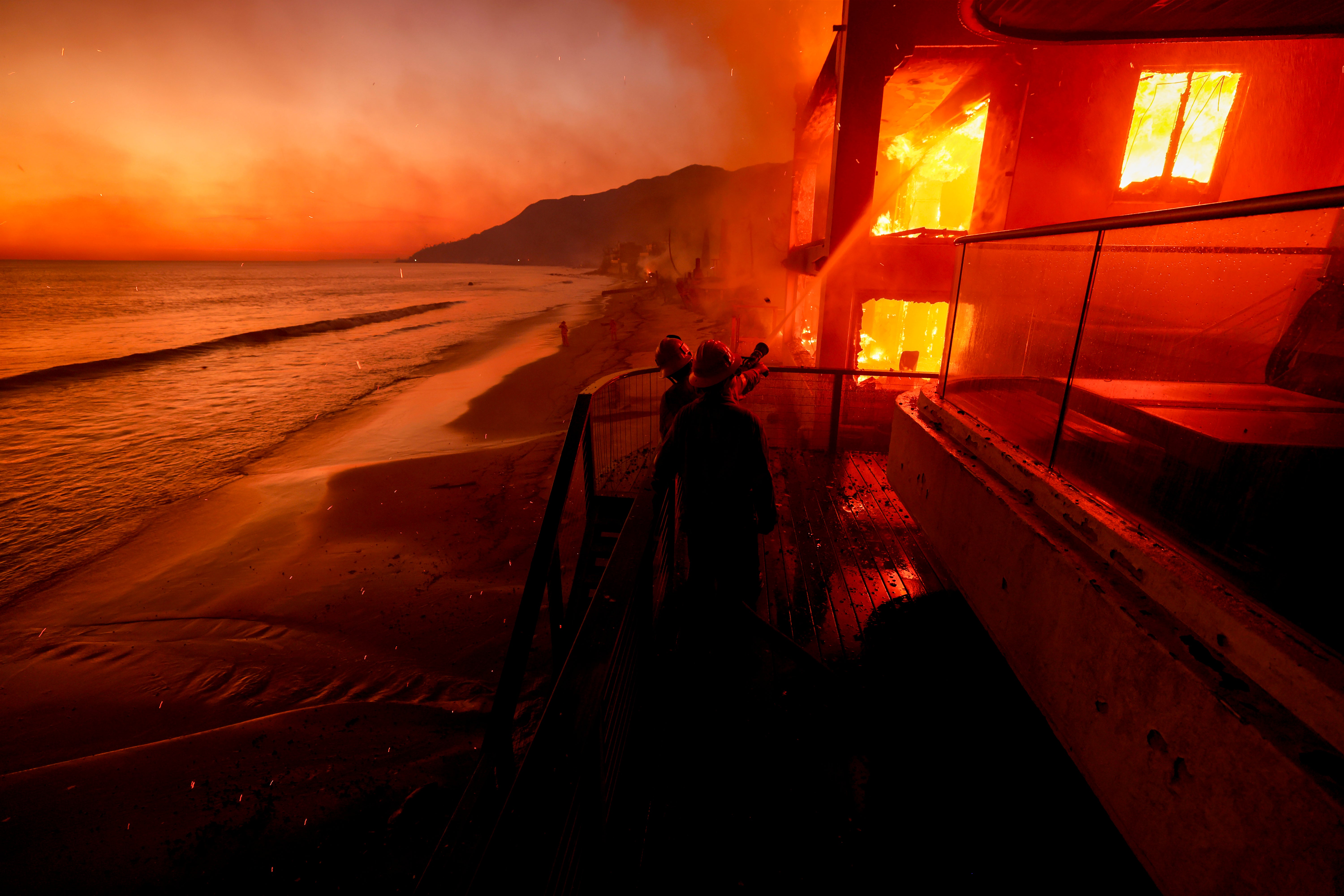 Firefighters work from a deck as the Palisades Fire burns a beachfront property on Wednesday, in Malibu, California. The blaze is still not contained