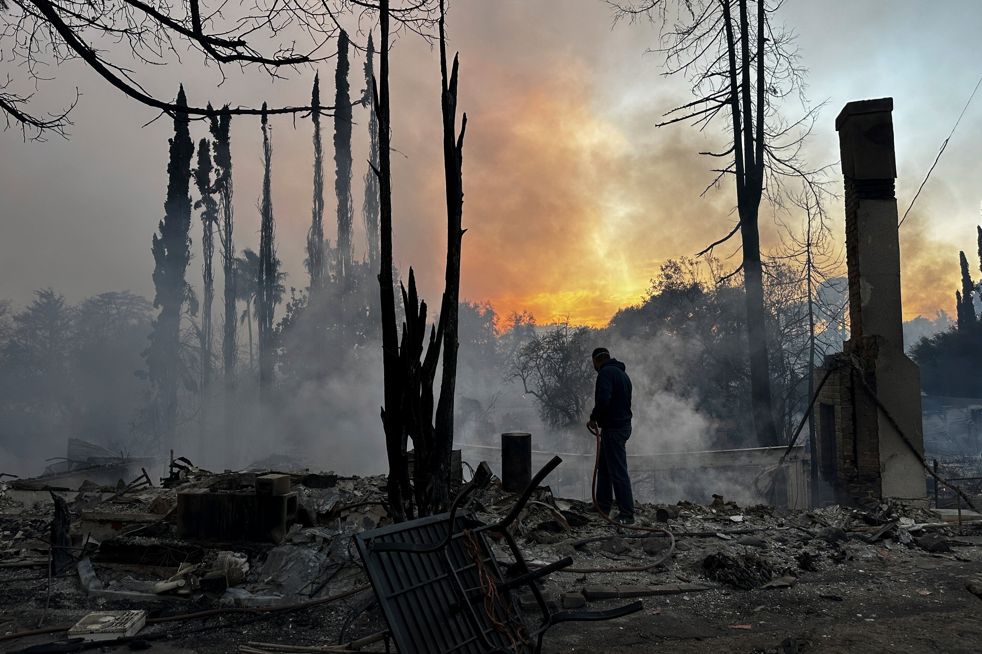 A resident hoses down hot spots in a fire-ravaged property in the Pacific Palisades neighborhood of Los Angeles, Wednesday, January 8, 2025