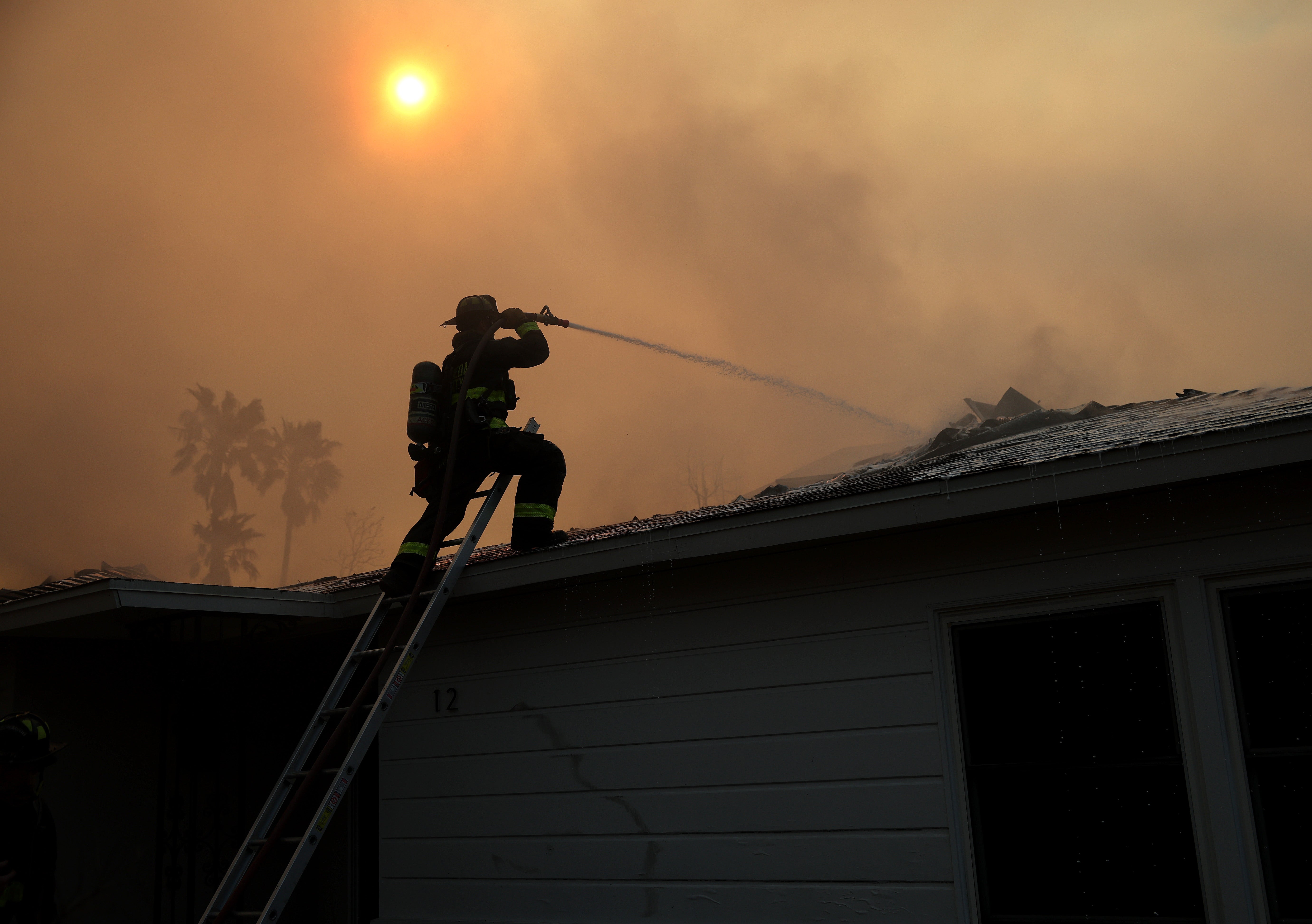 A firefighter sprays water on a burning home as the Eaton Fire moves through the area on Thursday in Altadena, California.