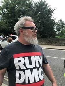 The other man is shown with grey hair, a beard and thick-rimmed glasses, wearing a t-shirt that has “Run DMC” written in large letters on the front