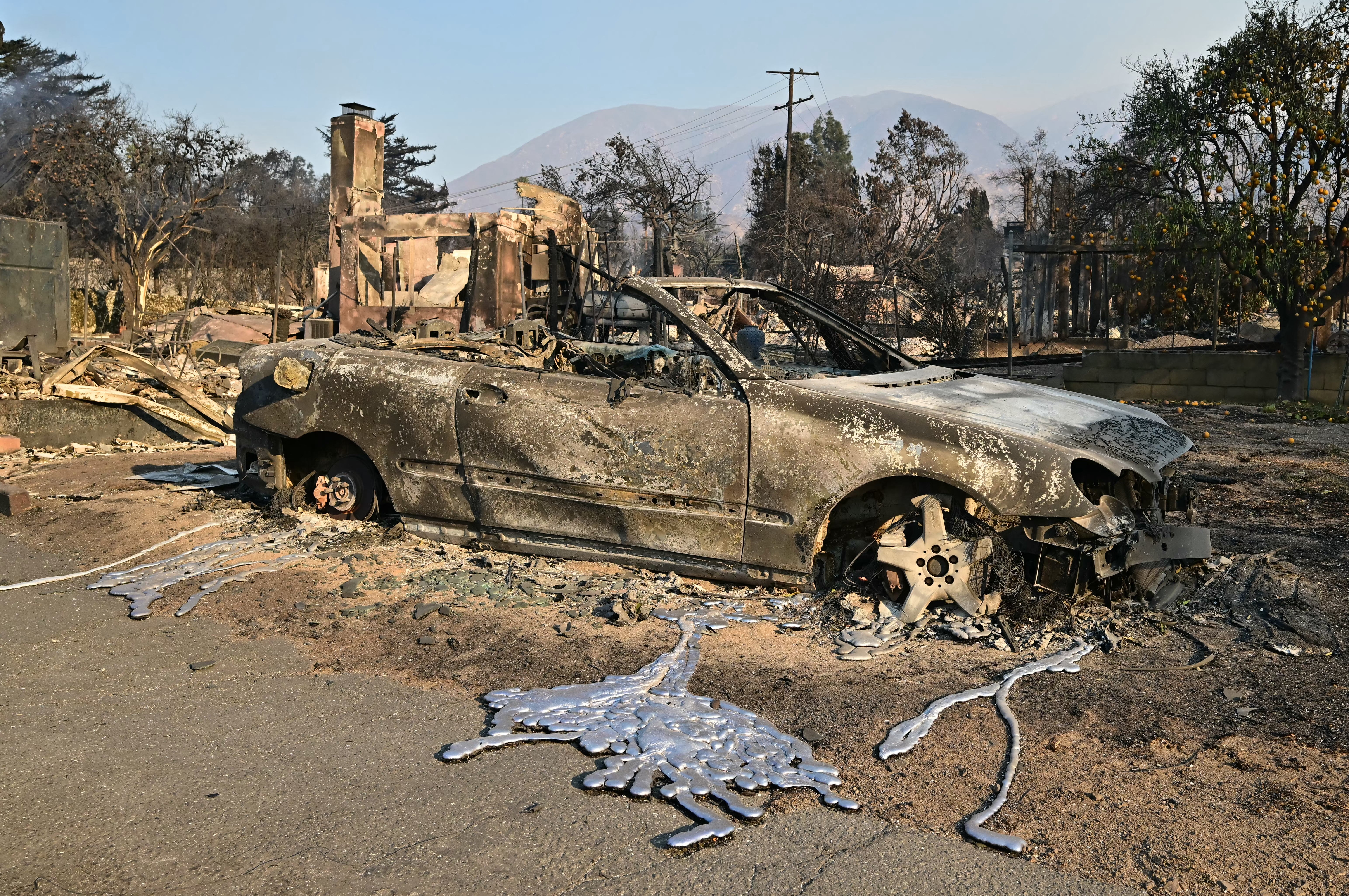 A partly melted car sits near burned-out homes destroyed by the Eaton Fire in Altadena, California, on Friday. Dangerous weather is expected to continue throughout the day