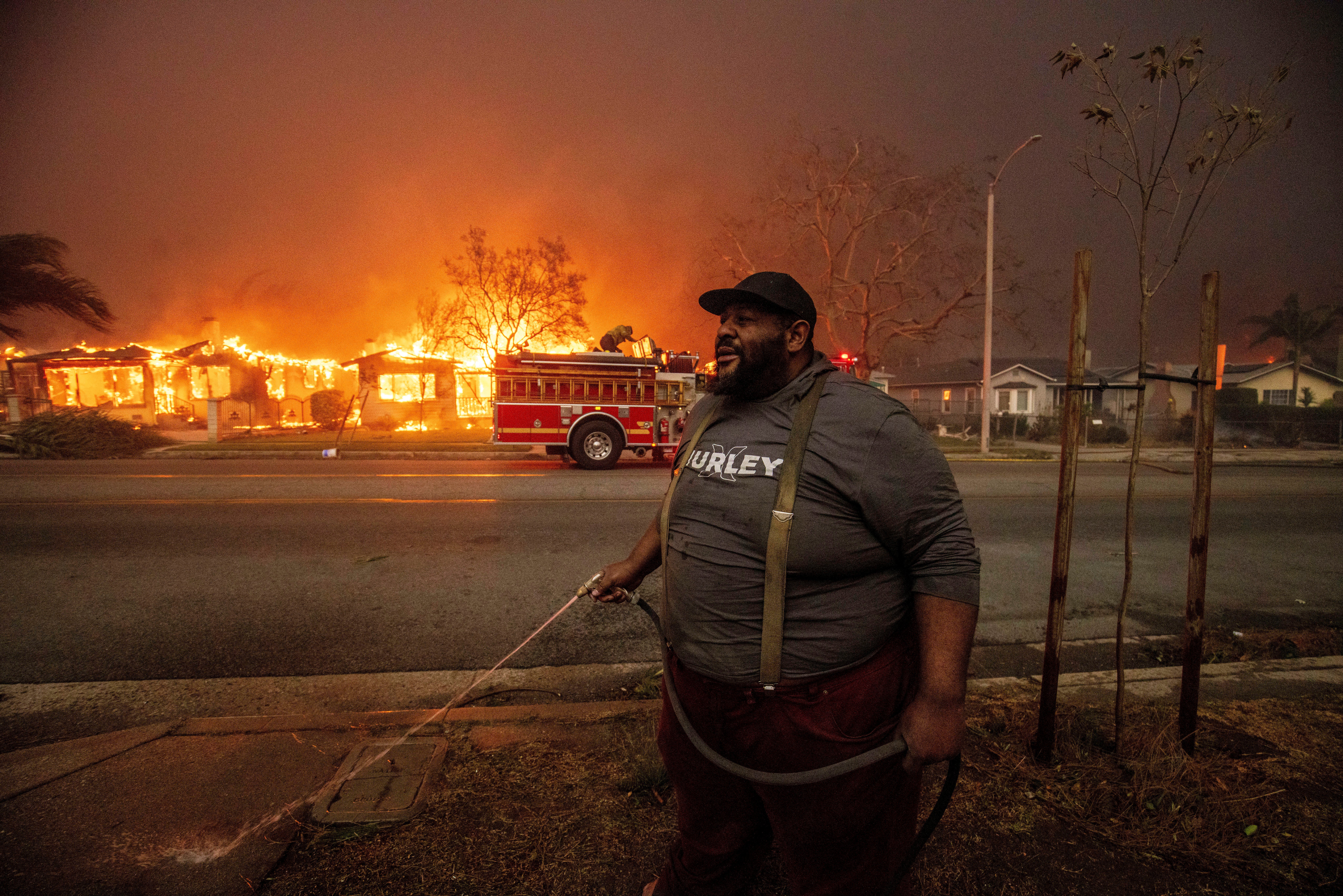 A resident sprays their property with a garden hose as the Eaton Fire engulfs structures across the street, in Altadena on January 8