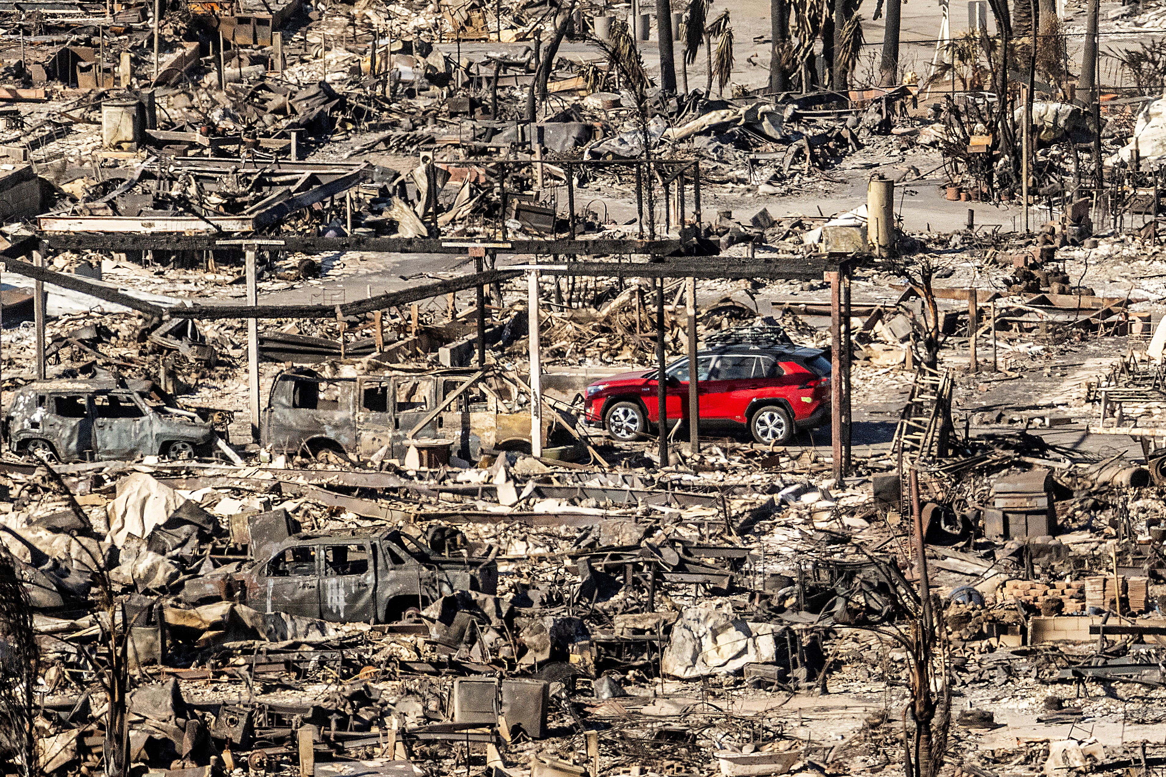 A car drives past homes and vehicles destroyed by the Palisades Fire on Sunday in Los Angeles, California. The Palisades Fire is the least contained