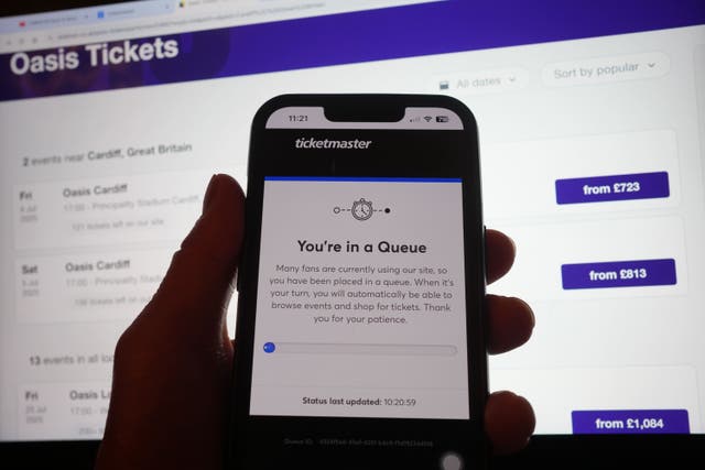 A person in a queue to access the Ticketmaster website on their phone, with the StubHub website in the background, detailing information about Oasis concert tickets for sale, in London (Yui Mok/PA)