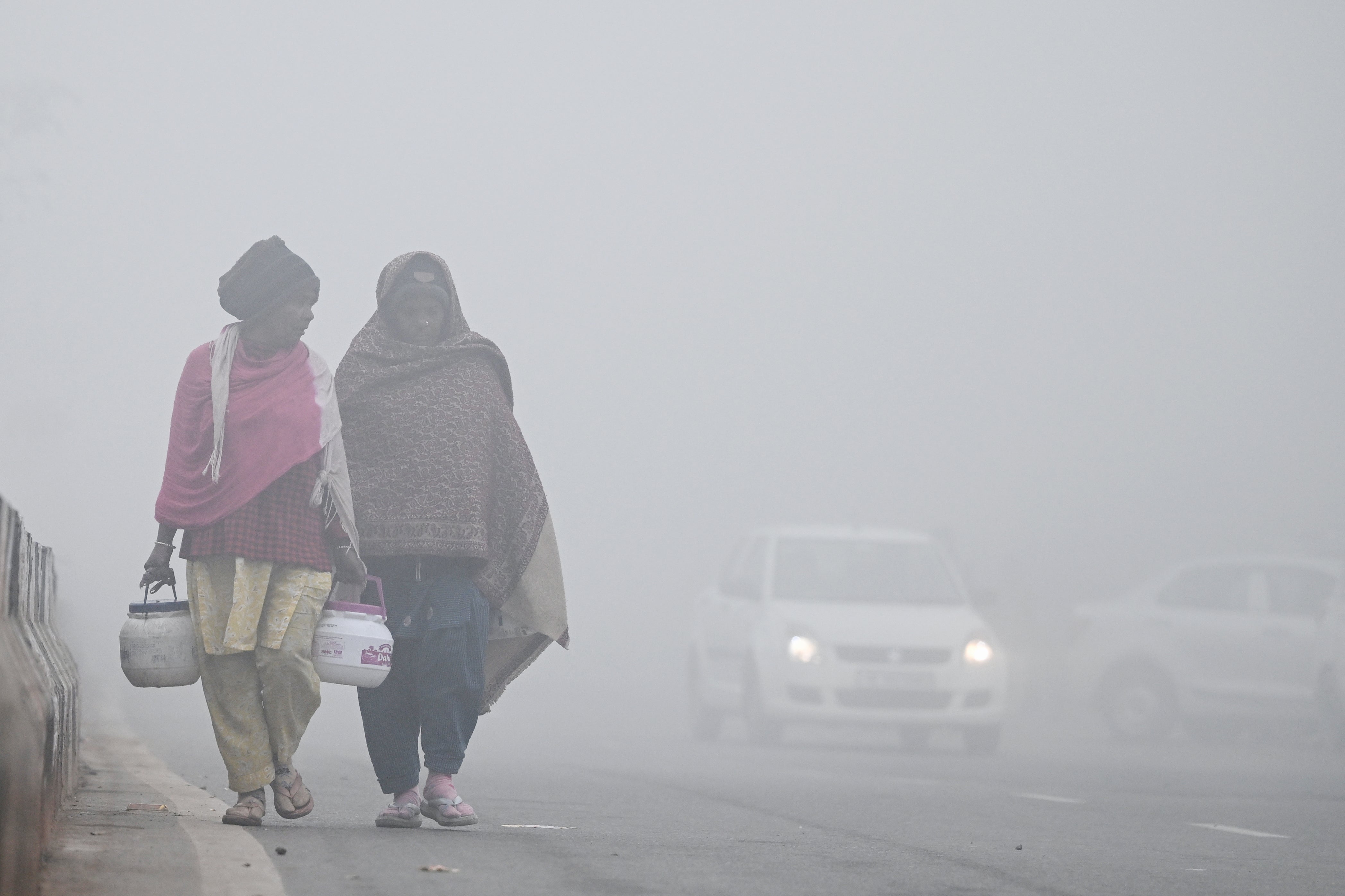 Pedestrians walk along a pavement amid dense fog on a cold winter morning in New Delhi