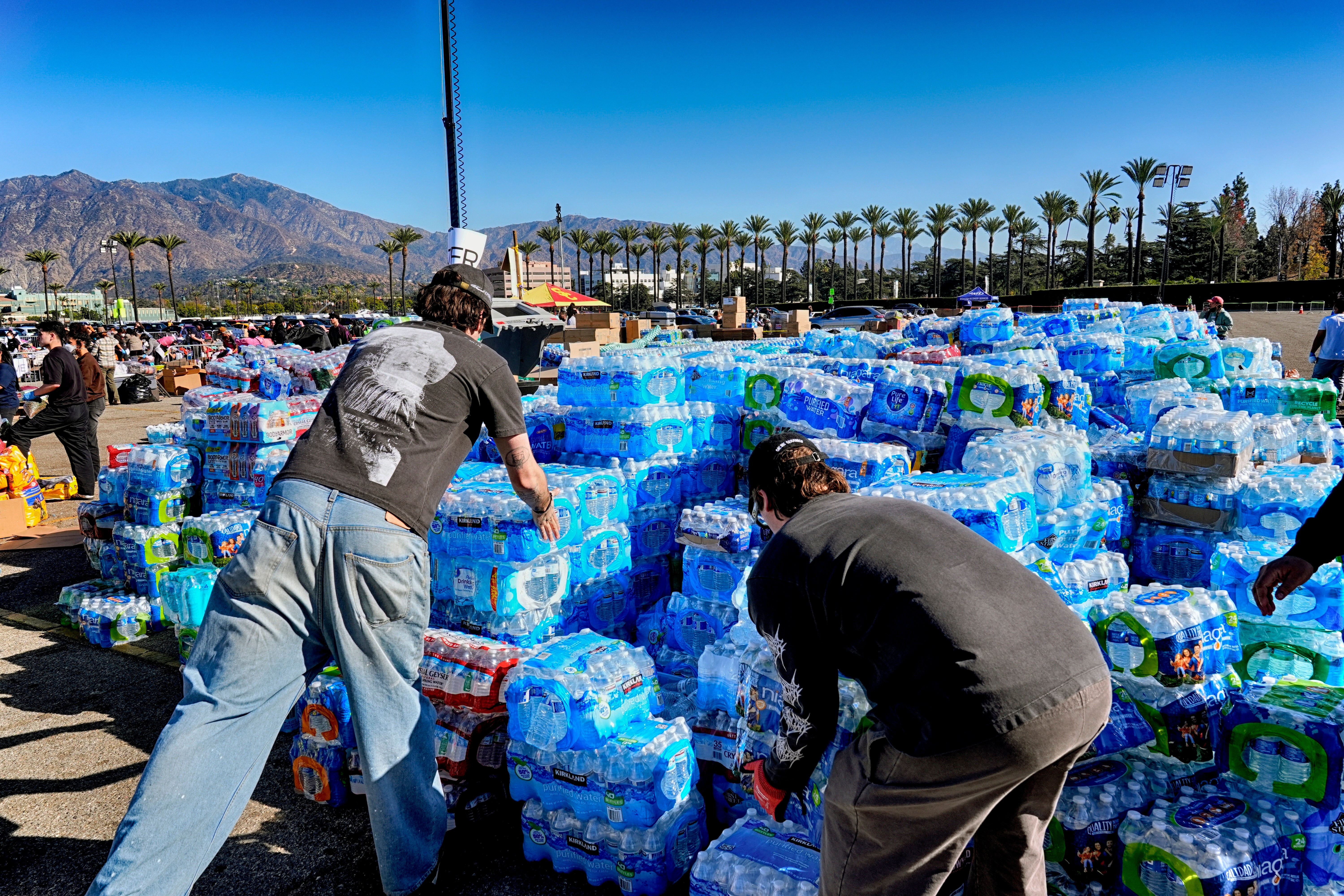 Volunteers stack donated water for people impacted by the Altadena Fire at a donation center at Santa Anita Park in Arcadia, California, on Wednesday. The county said in-kind donations are at capacity