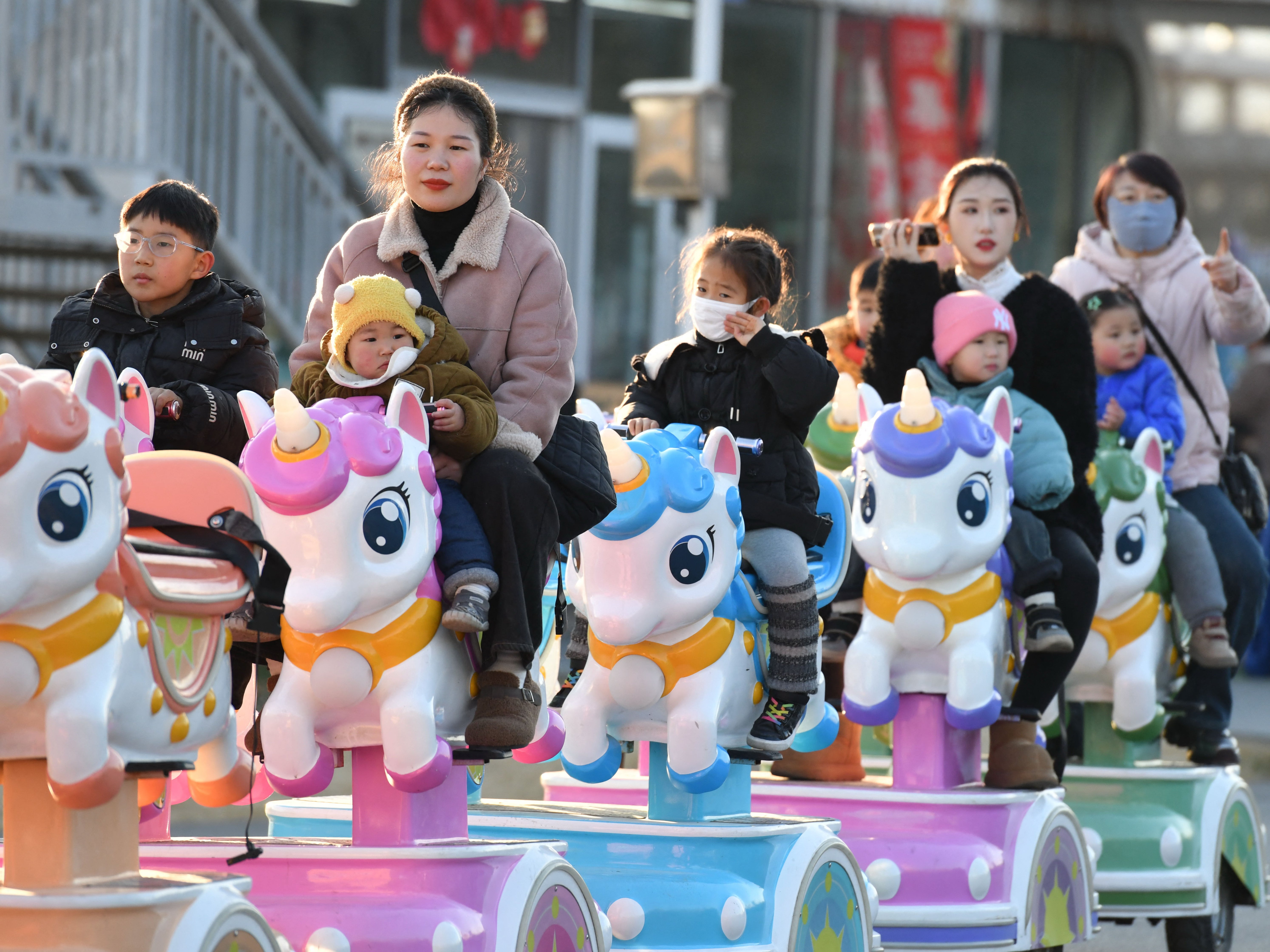 <p>This photo taken on 16 January 2025 shows children taking a ride with adults in a park in Fuyang, east China’s Anhui province. China said on 17 January its population fell for the third year running in 2024, extending a downward streak after more than six decades of growth as the country battles a looming demographic crisis</p>