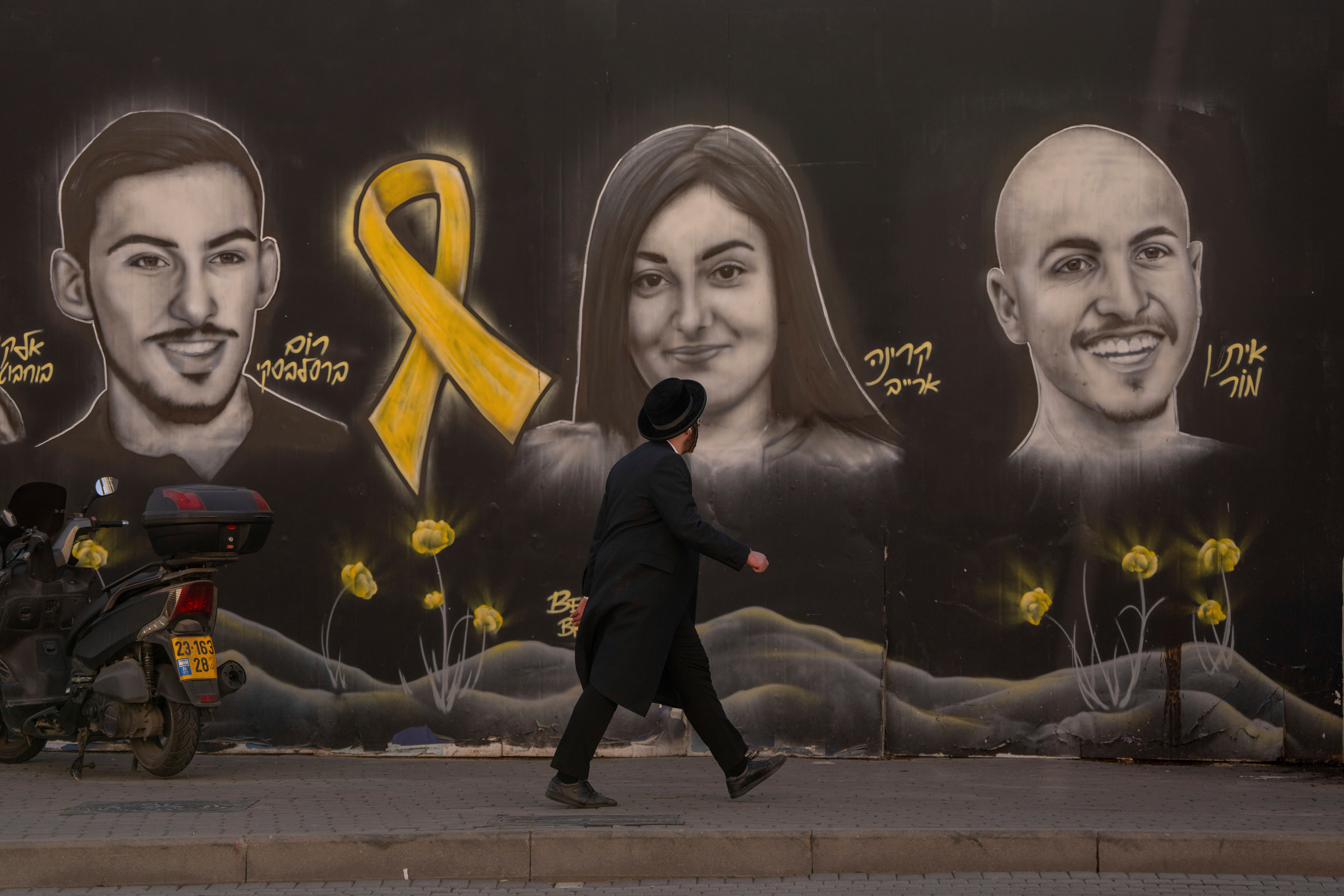 An Ultra-orthodox Jewish man walks past graffiti portraits in Jerusalem of hostages held by Hamas in Gaza (Ohad Zwigenberg/AP)