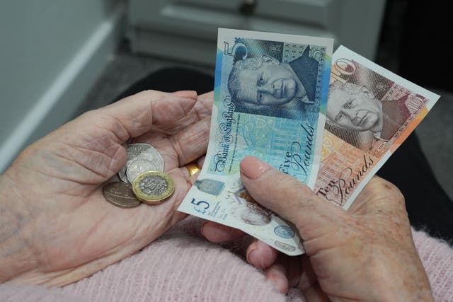 An old age pensioner holding bank notes and coins at home (PA)