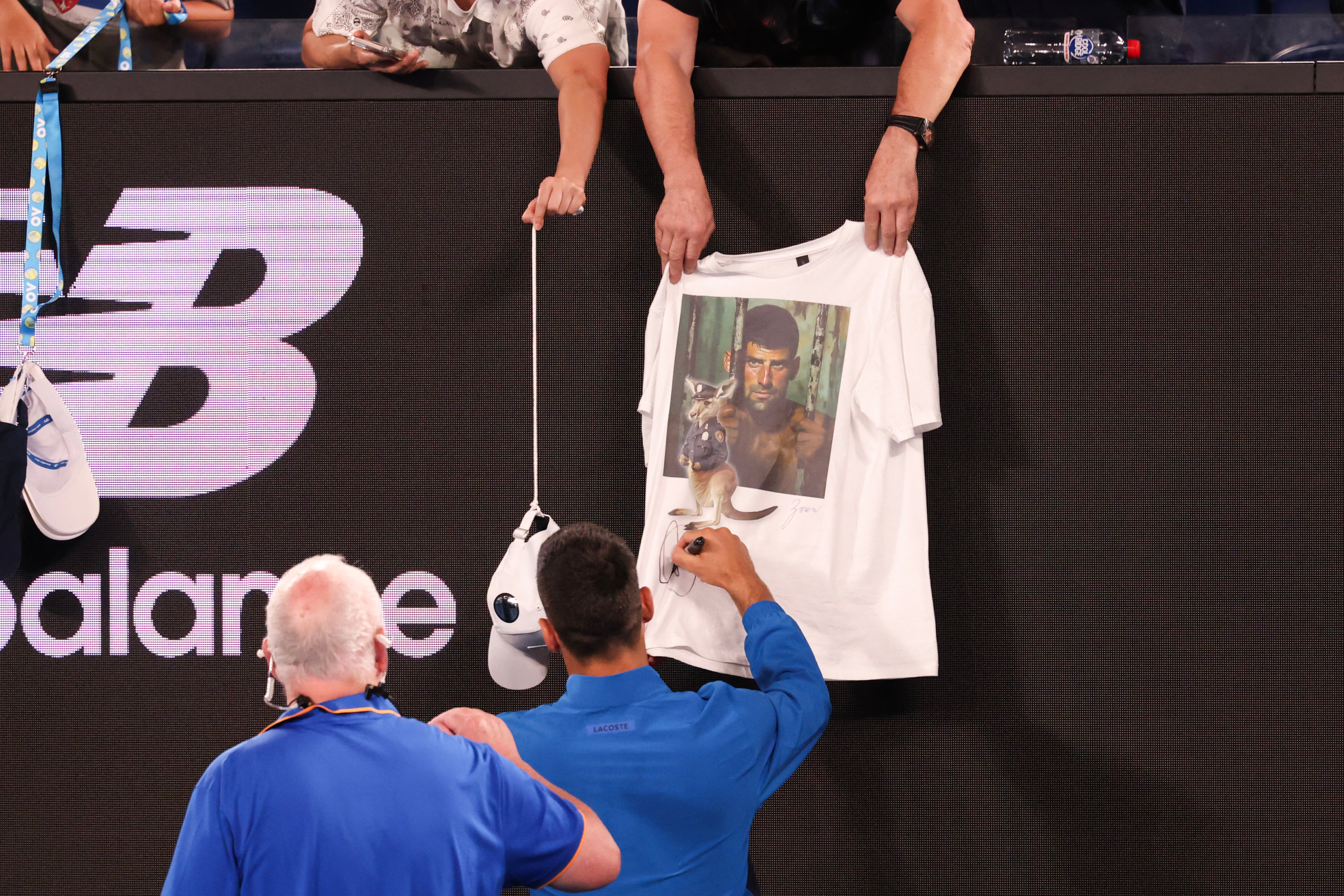 Serbia's Novak Djokovic signs a fan's t-shirt depicting him behind bars