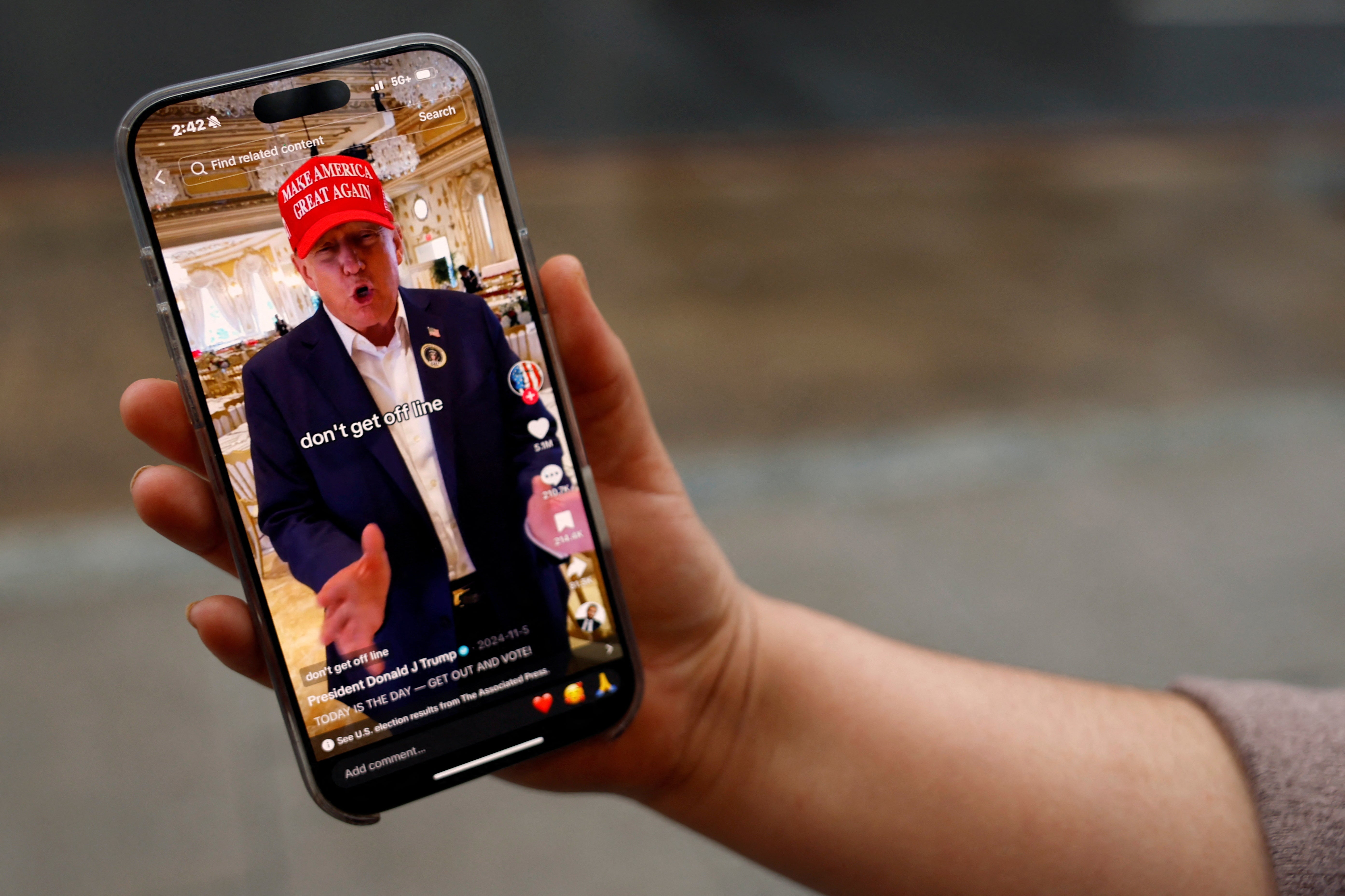 <p>A woman poses with her smartphone displaying the @realdonaldtrump TikTok page</p>
