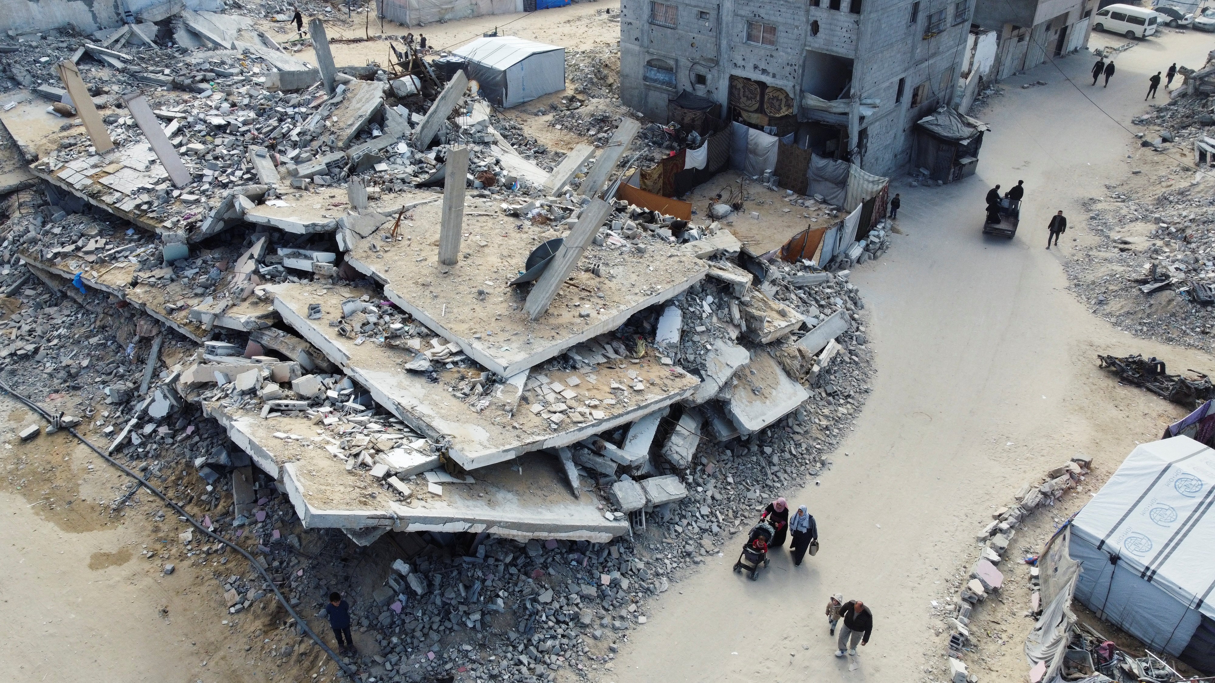 Palestinians walk past the rubble of houses and buildings destroyed in Israeli strikes during the war