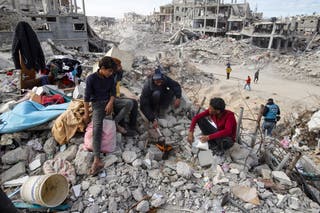 Displaced Palestinians gather around a fire next to their destroyed home in Rafah in the Gaza Strip on Monday