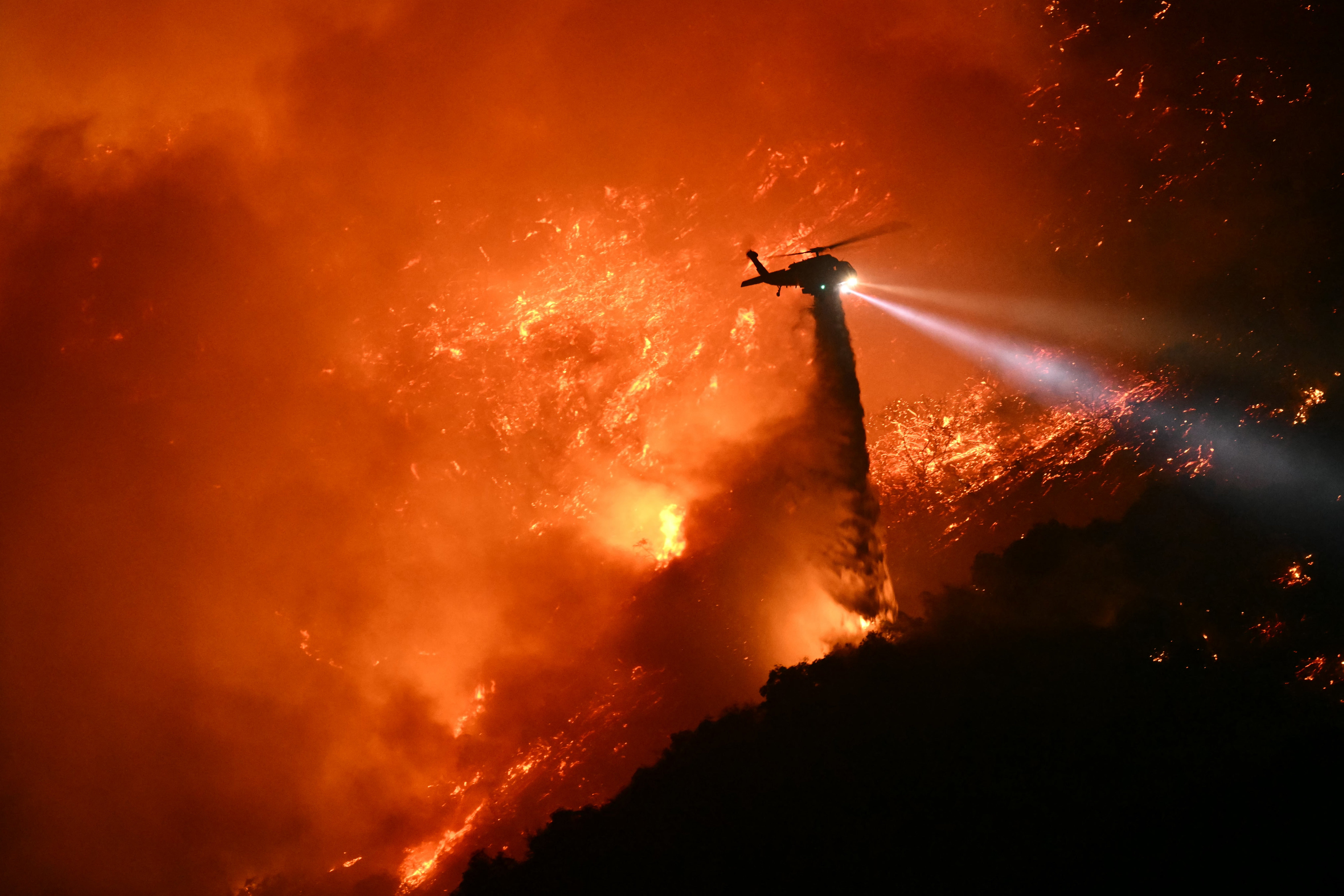 A firefighting helicopter drops water as the Palisades Fire grows near Encino, California, earlier this month. Firefighters are still fighting the blaze, which is now nearly 60 percent contained