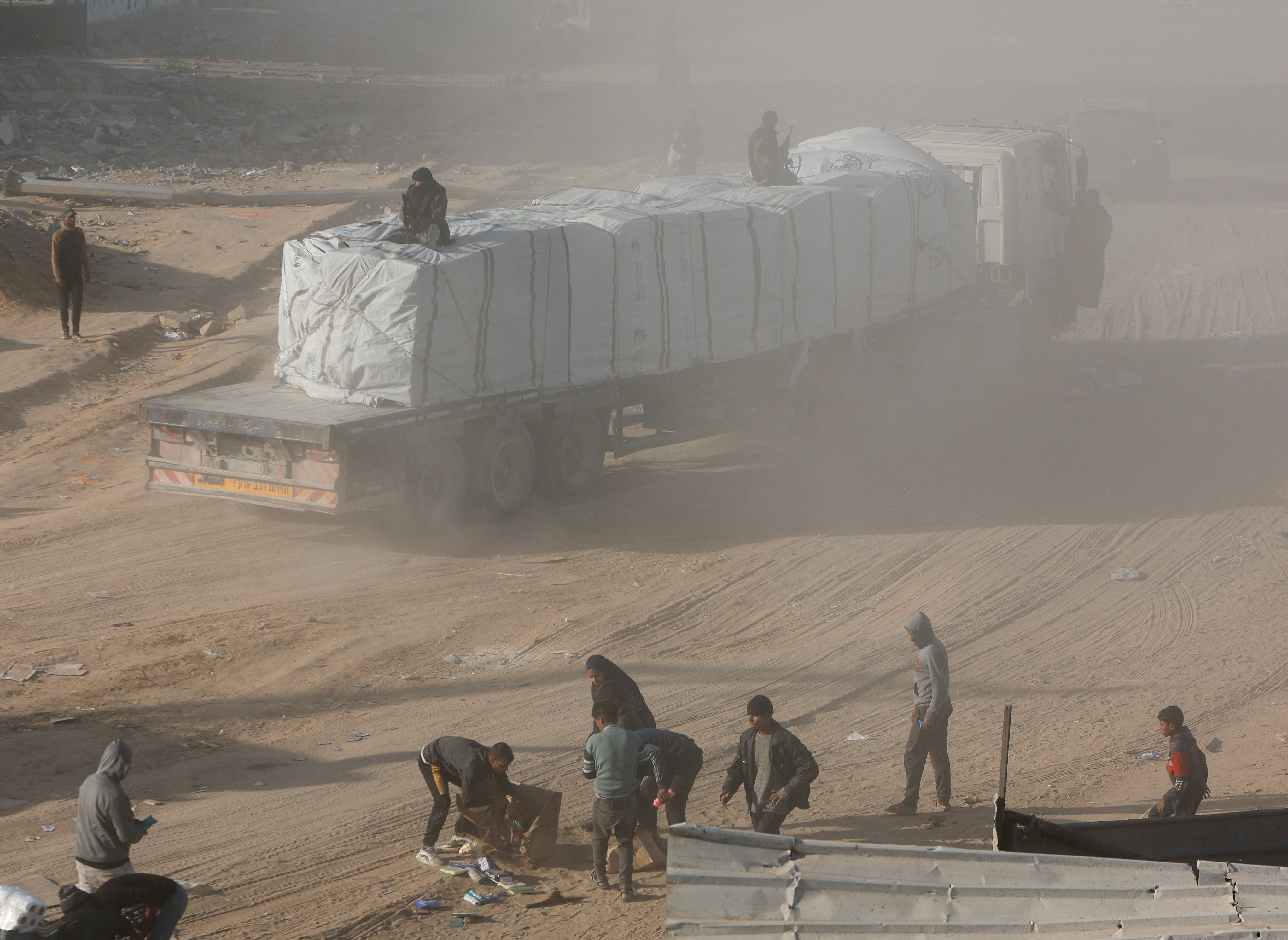 Palestinians rush to collect aid taken from moving trucks entering Rafah, following a ceasefire between Israel and Hamas, in the southern Gaza Strip, 20 January 2025