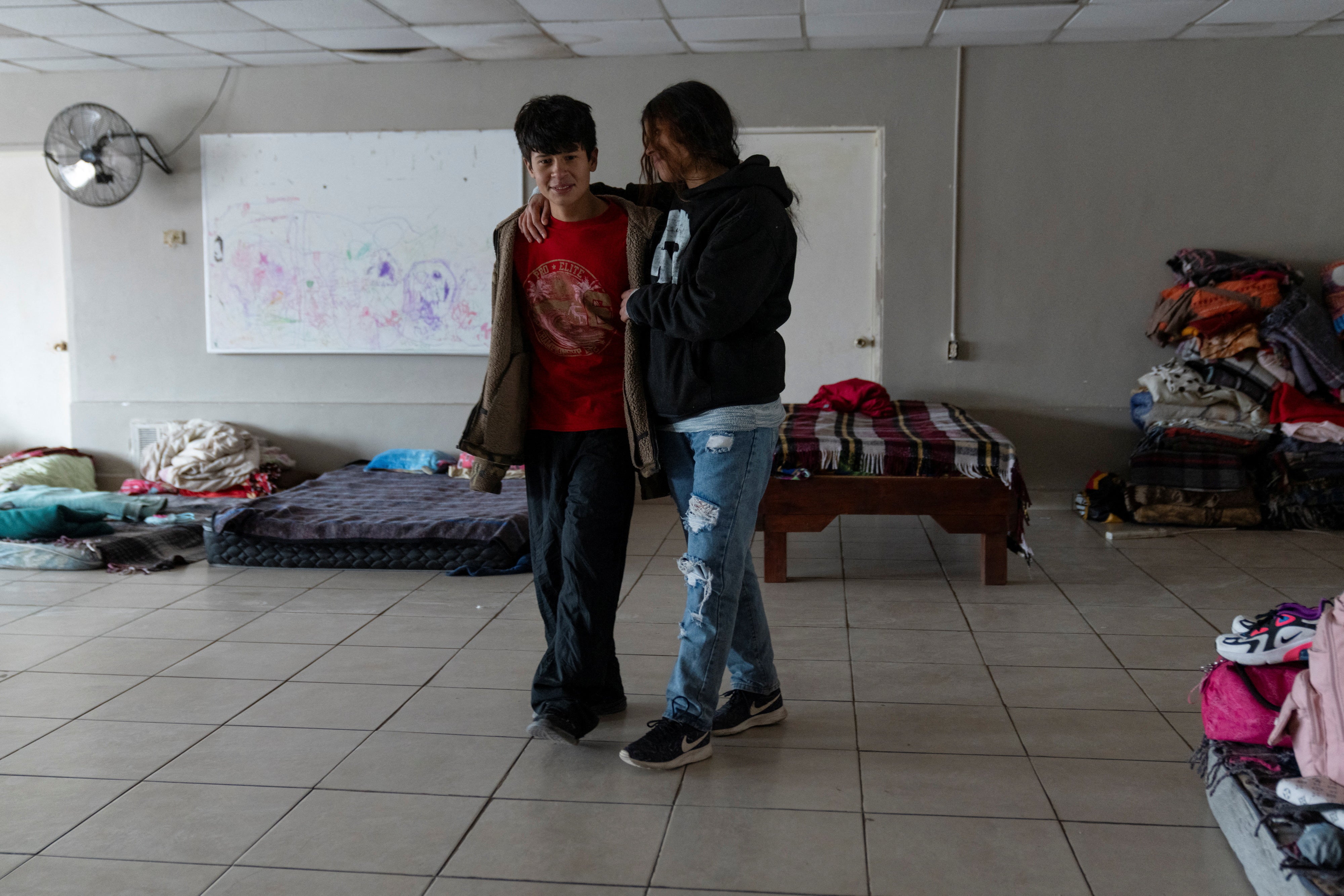 Sofia Mendez, 15, and her brother Isai, 13, walk through the sleeping quarters of a migrant shelter