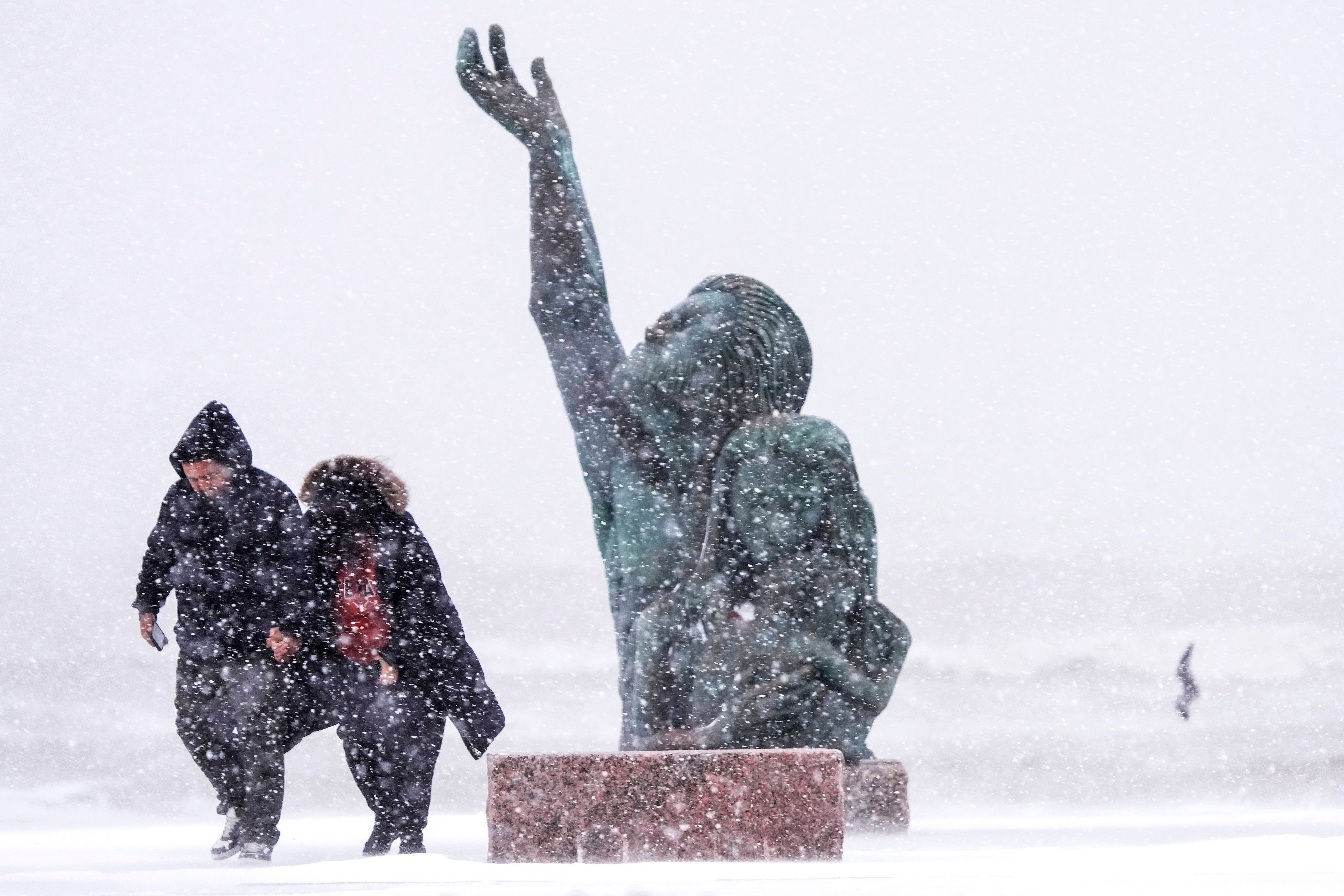 People walk past the 1900 Storm memorial sculpture during an icy winter storm on Tuesday in Galveston, Texas. Galveston roads were deemed to be hazardous