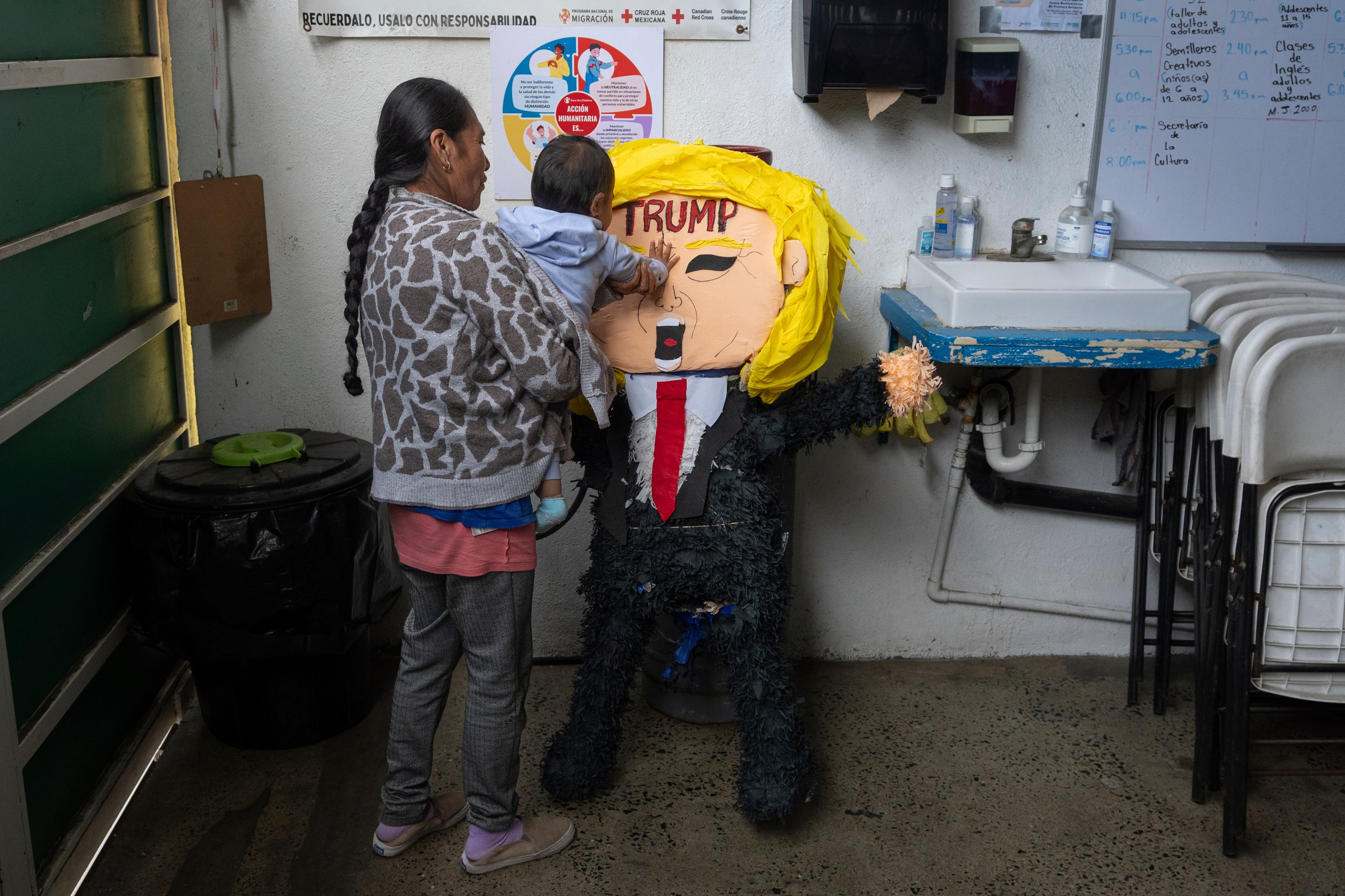 A migrant woman from the Mexican state of Guerrero holds her 1-year-old granddaughter as she hits a piñata of President Donald Trump at a shelter for migrants Wednesday