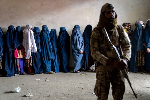 <p>A Taliban fighter stands guard as women wait to receive food rations distributed by a humanitarian aid group in Kabul, Afghanistan</p>