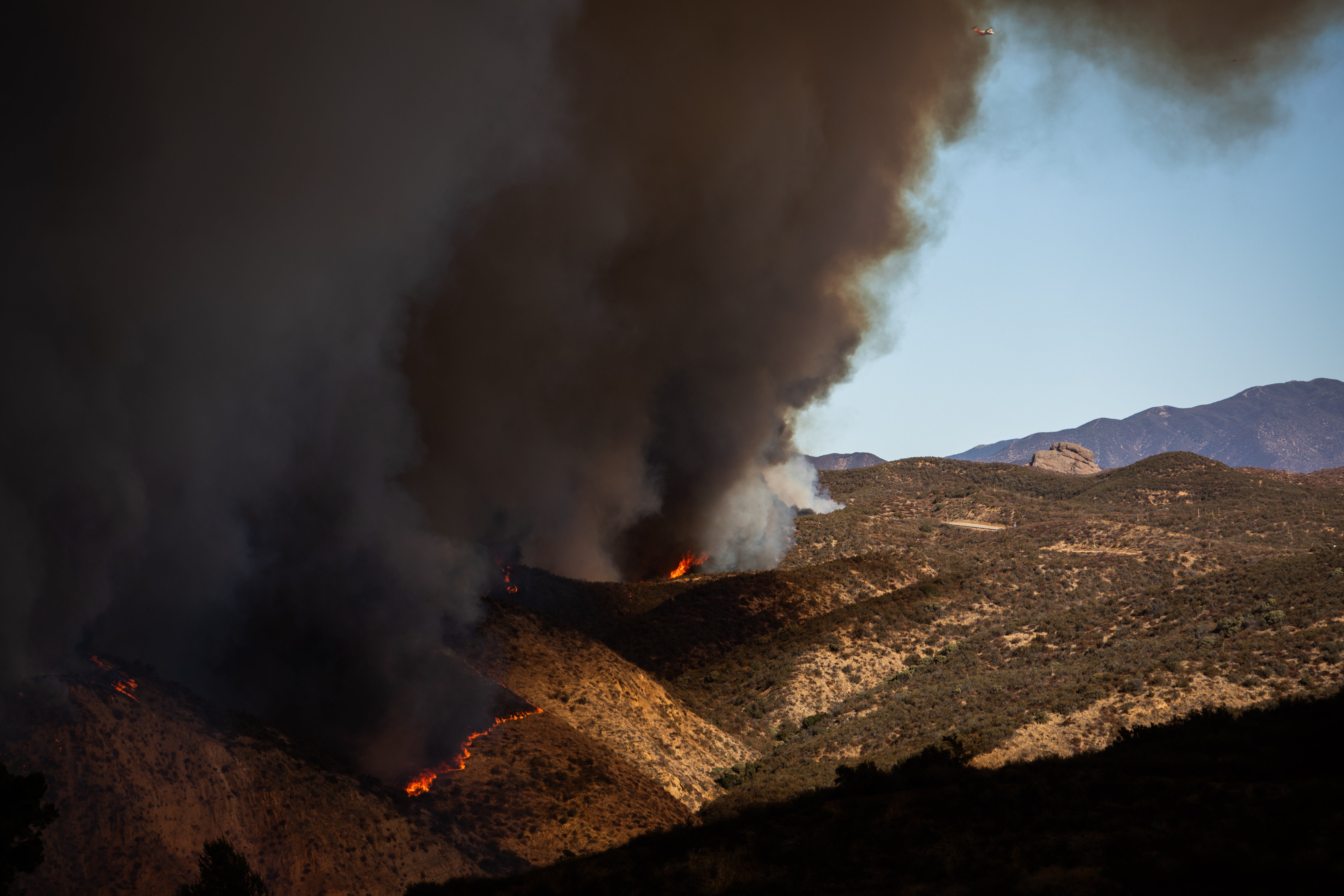 Flames race up the hill as the plume of smoke from the Hughes fire fills the sky in Castaic, California, on Wednesday. The fire is still just 14 percent contained