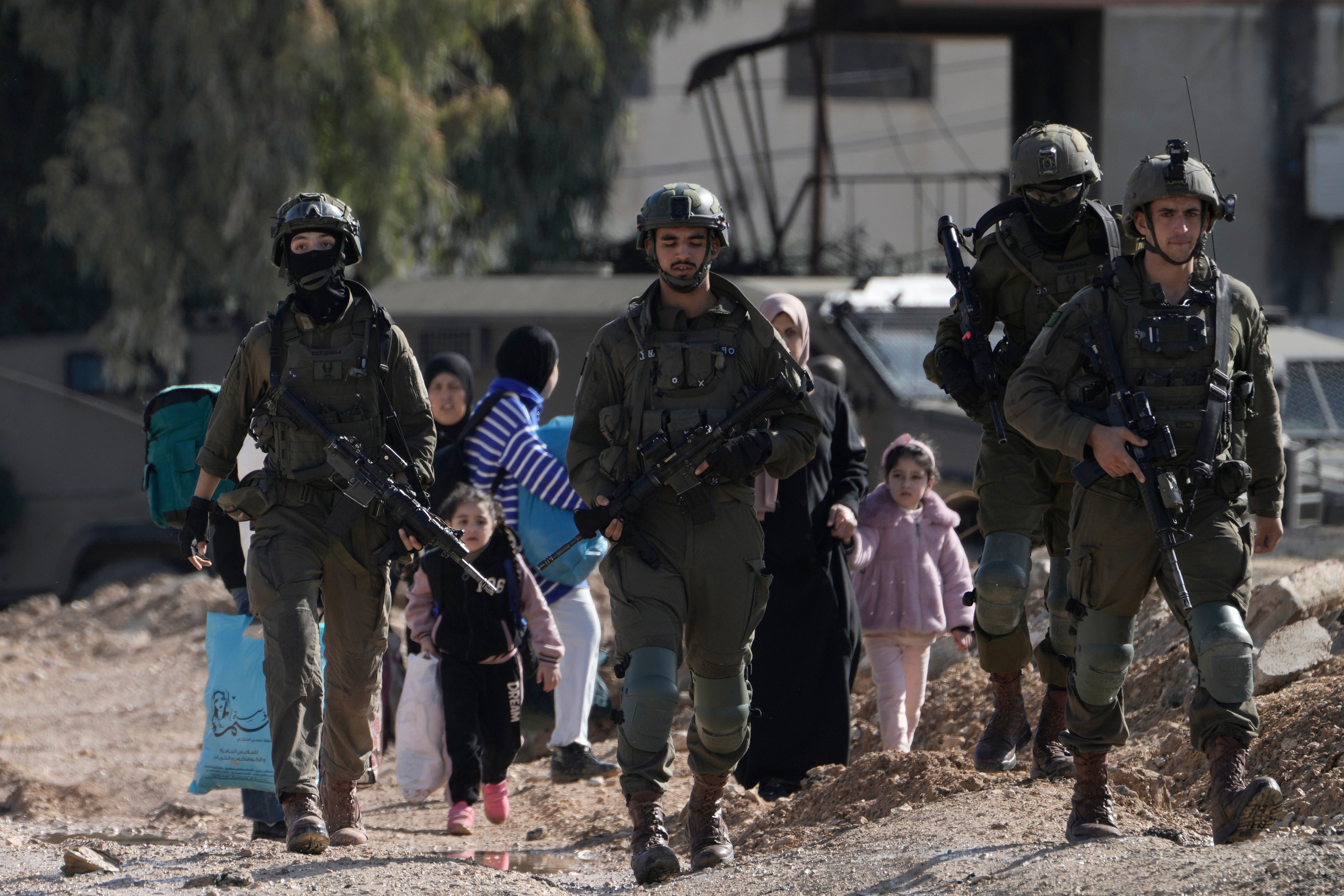 IDF soldiers walk ahead of Palestinians displaced by an Israeli military operation and evacuating from the Jenin refugee camp in the West Bank on Thursday 23 January 2025