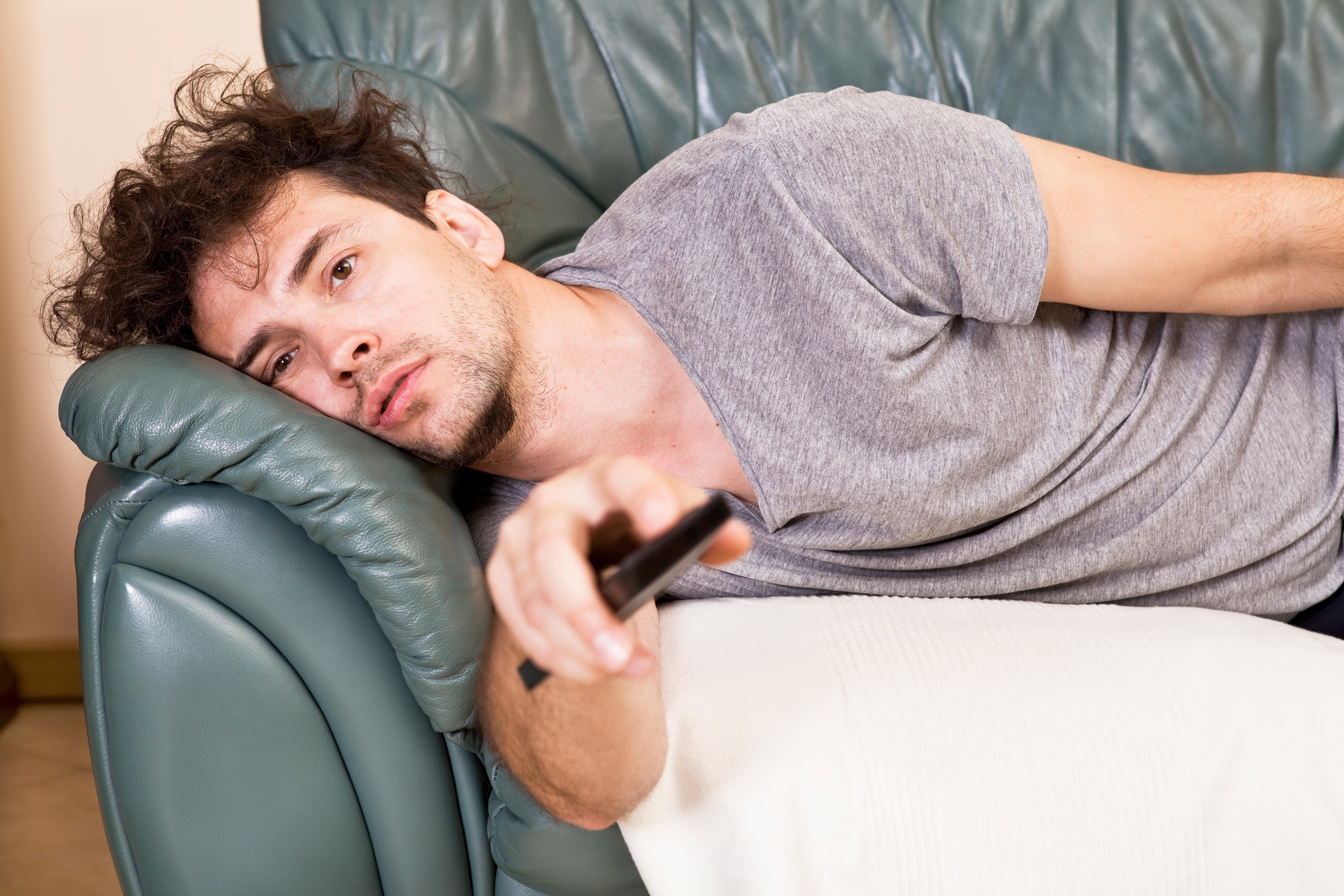 Man laying on a sofa pointing a remote control at the TV