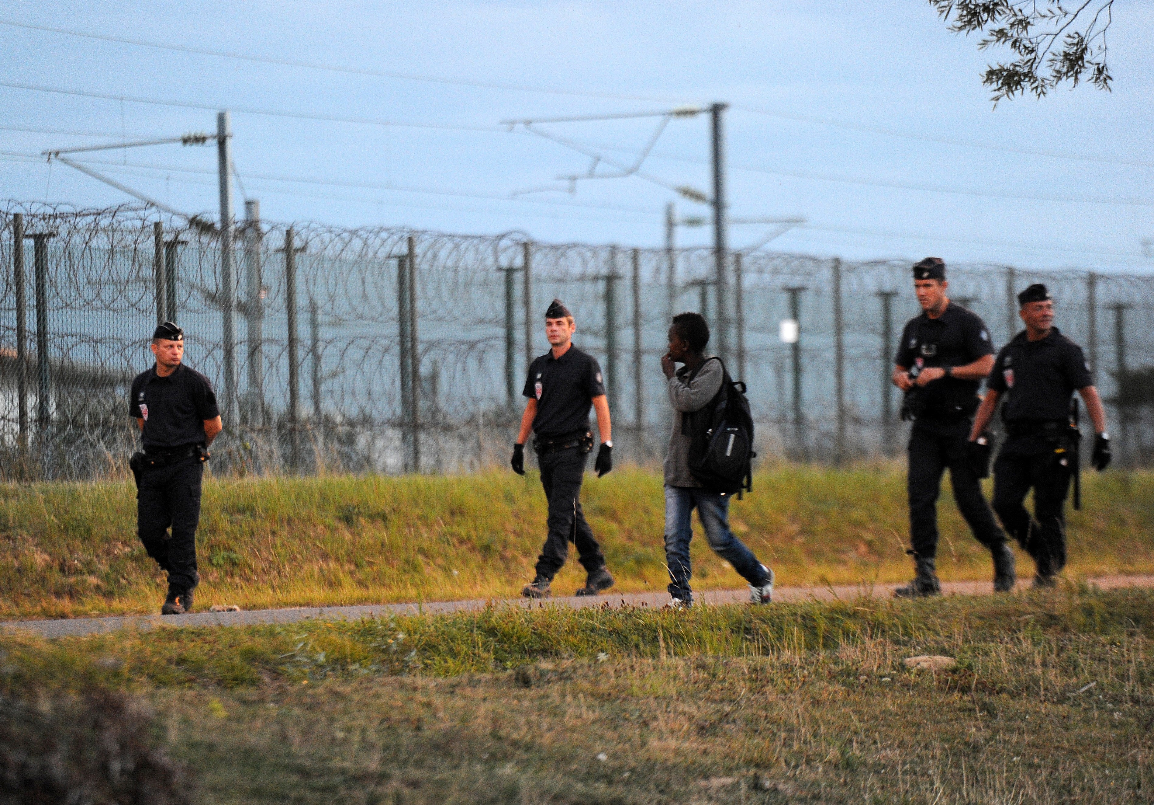 Police officers follow a young migrant in Coquelles near the northern French port of Calais as part of security efforts to stop migrants from reaching the Eurotunnel terminal in August 2015