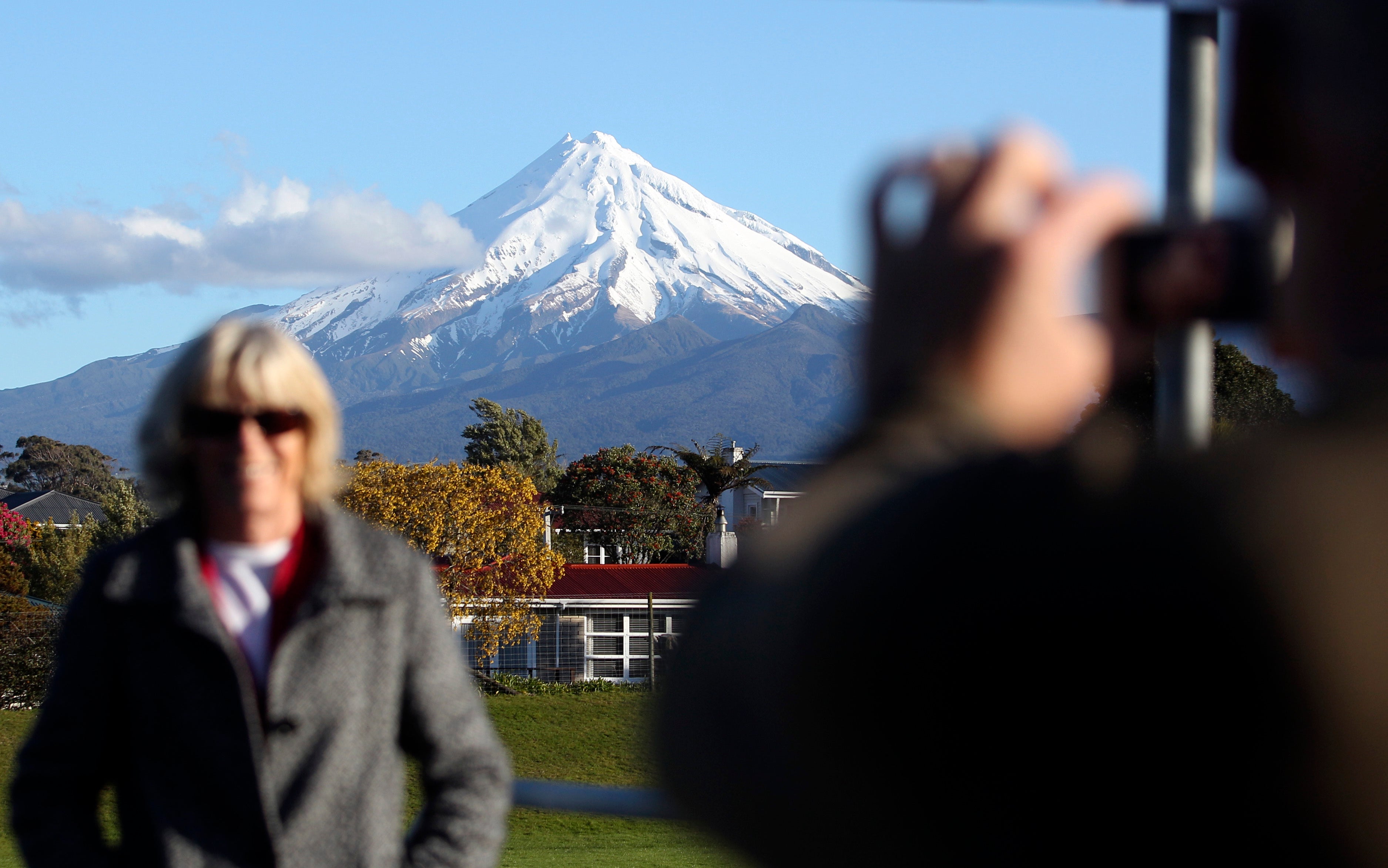 A man takes a picture of his wife with Mount Taranaki, also known as Mount Egmont, in the background in New Plymouth, New Zealand, Sept. 26, 2011