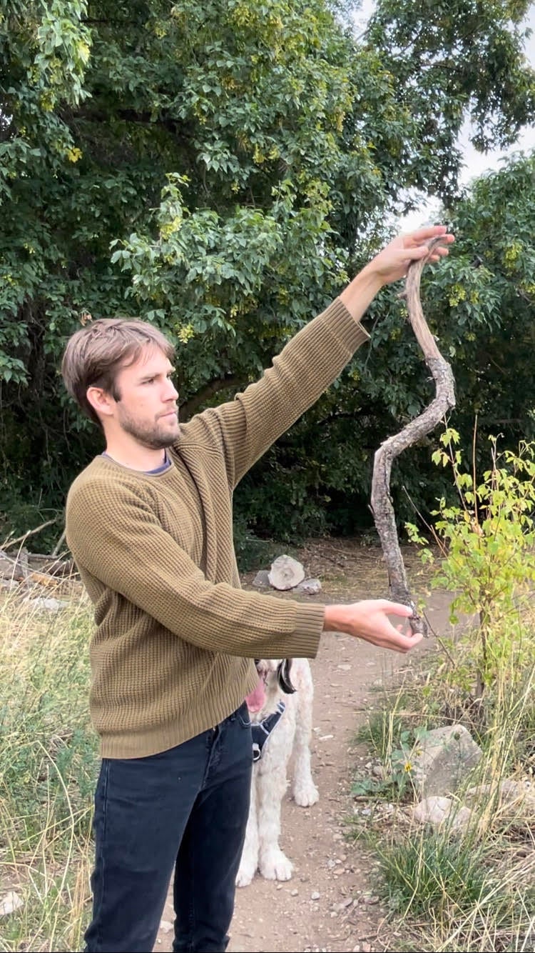 Boone Hogg holds a shorter, curved stick while out in nature. They receive hundreds of stick submissions every day