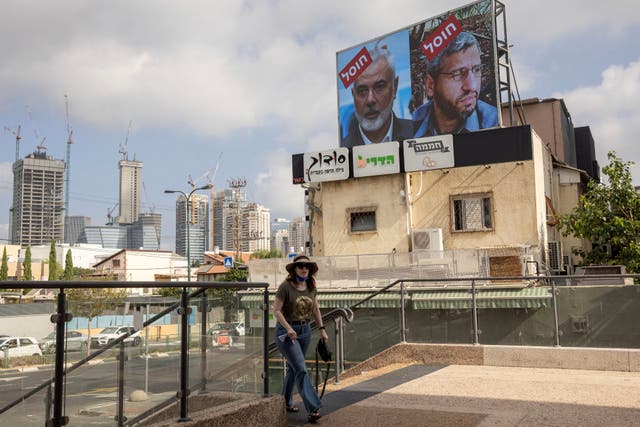 <p>A woman walks near a billboard displaying portraits of Hamas leader Mohammed Deif (R) and Ismail Haniyeh with the slogan 'assassinated' reading in Hebrew, in Tel Aviv</p>