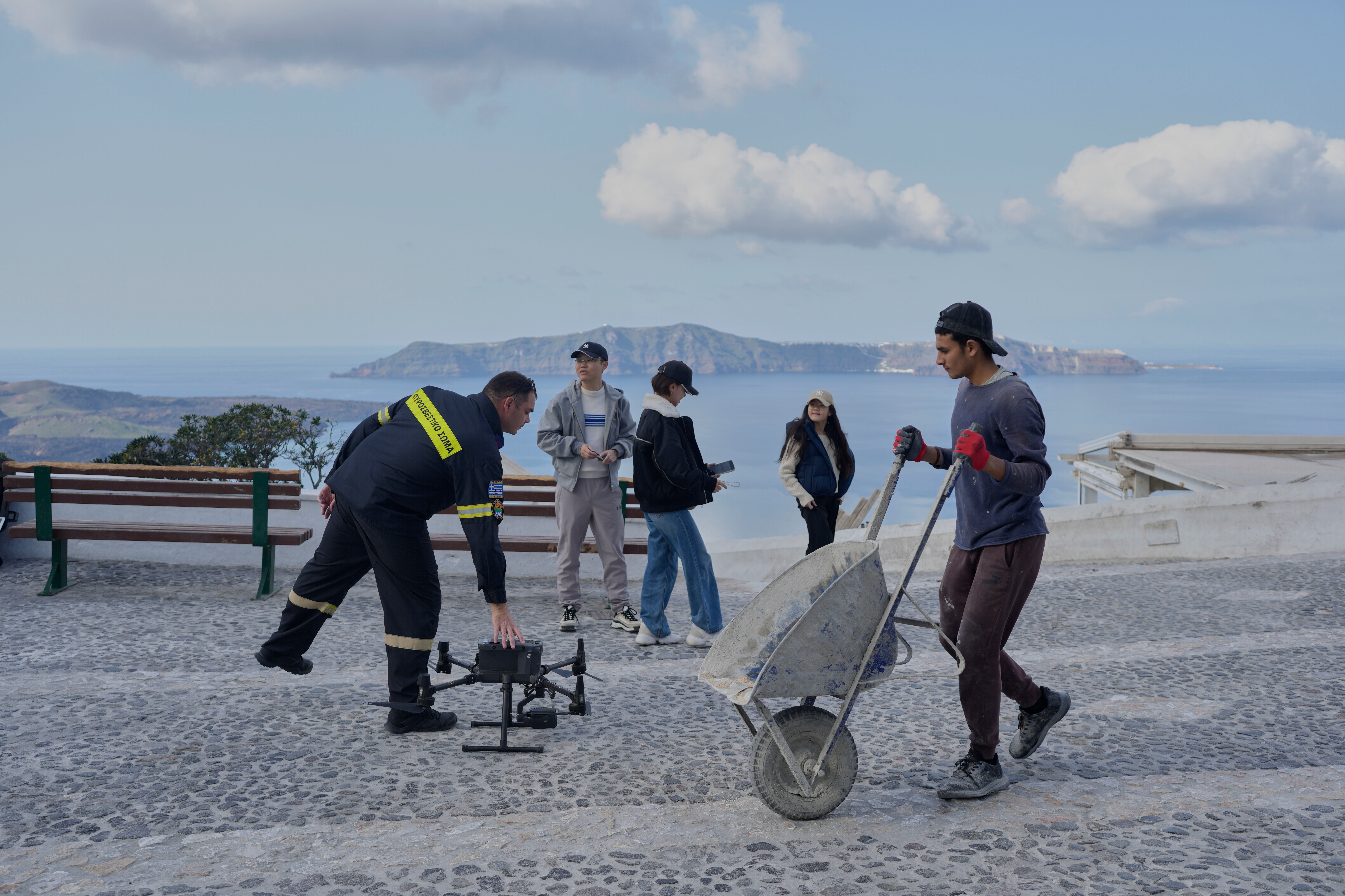 A firefighter controls a drone next to tourists after emergency crews were deployed to the island as Greek authorities are taking emergency measures in response to intense seismic activity on the popular Aegean Sea holiday island of Santorini, southern Greece, Monday, Feb. 3, 2025. (AP Photo/Petros Giannakouris)