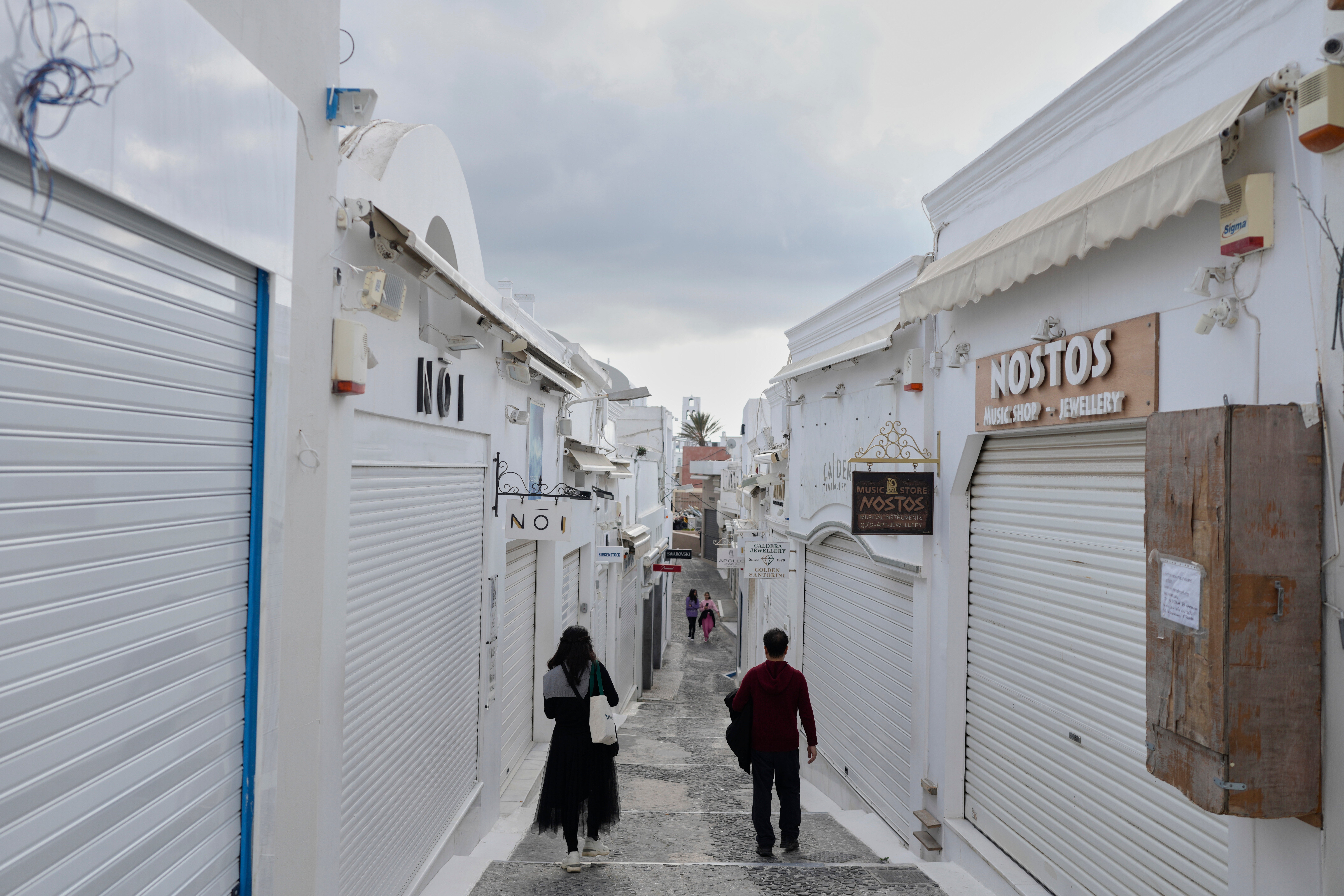 <p>Tourists pass by closed shops in Fira town as Greek authorities are taking emergency measures in response to intense activity </p>