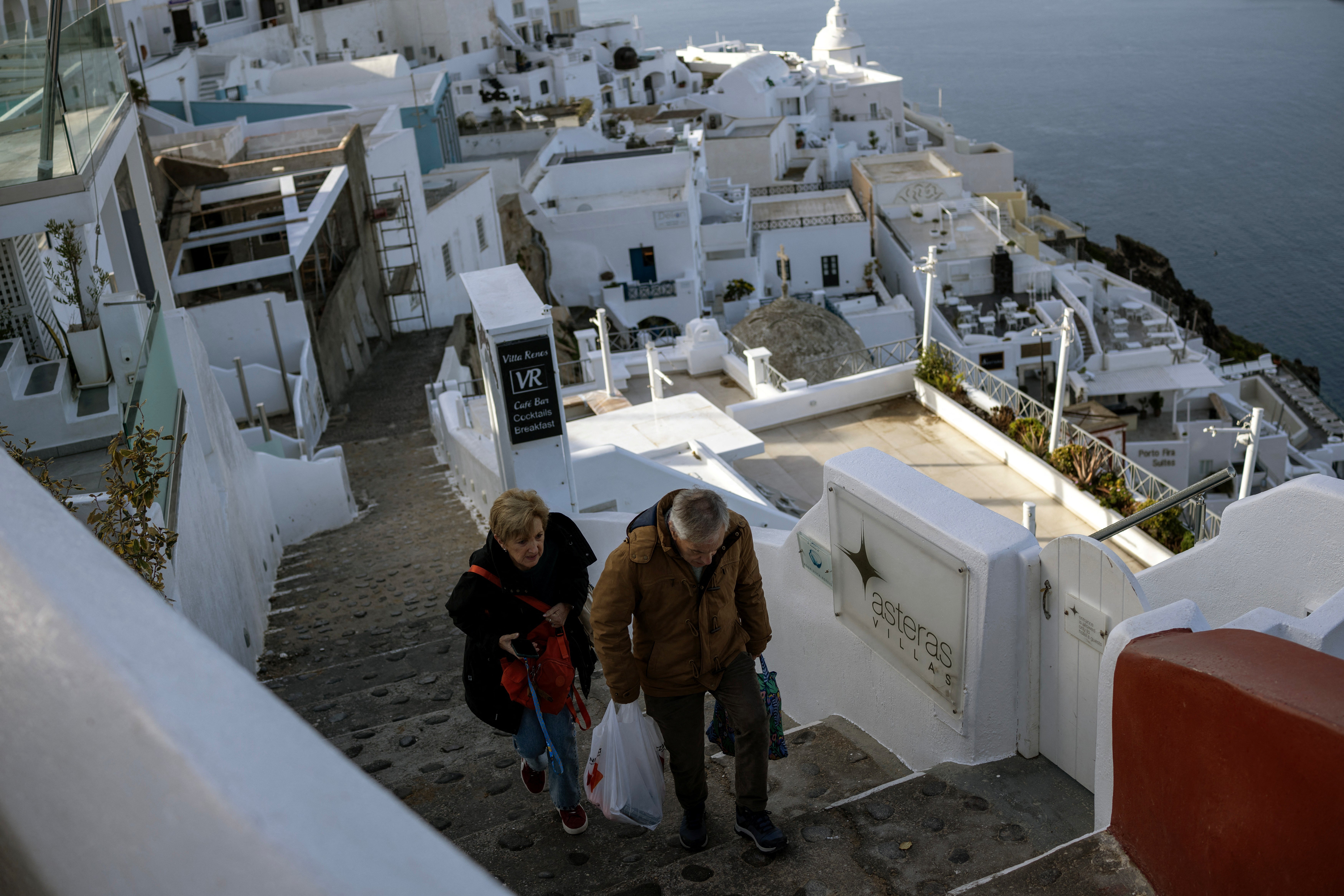 Tourists carry their luggage as they leave the village of Fira