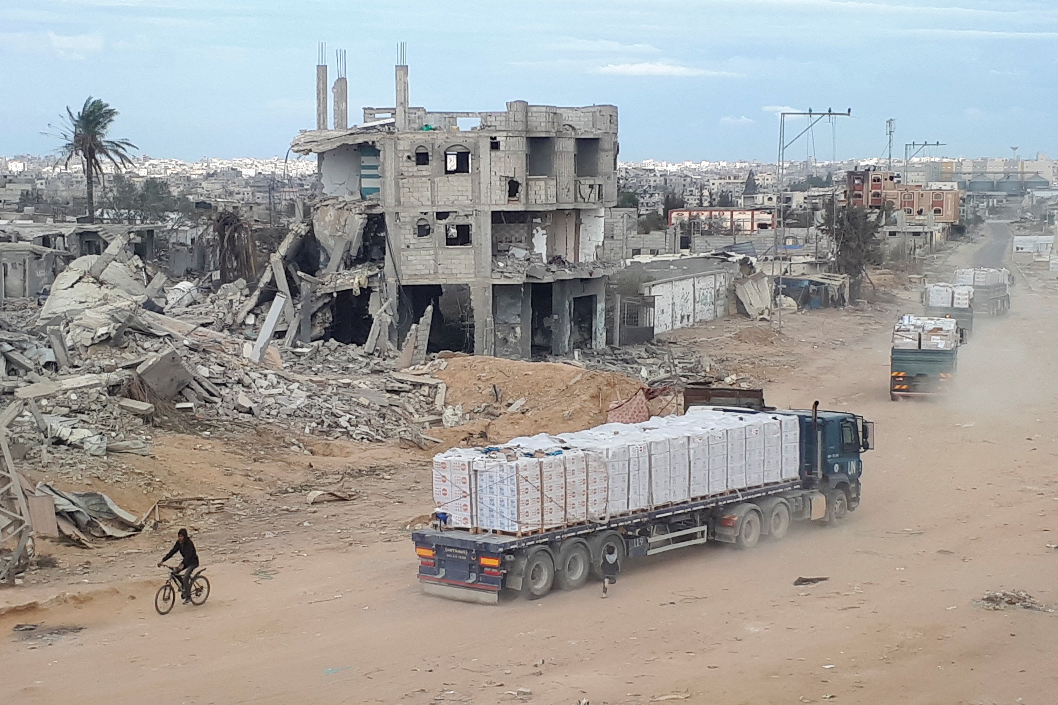<p>Wish you were here…?: Aid trucks drive past flattened buildings in Gaza</p>