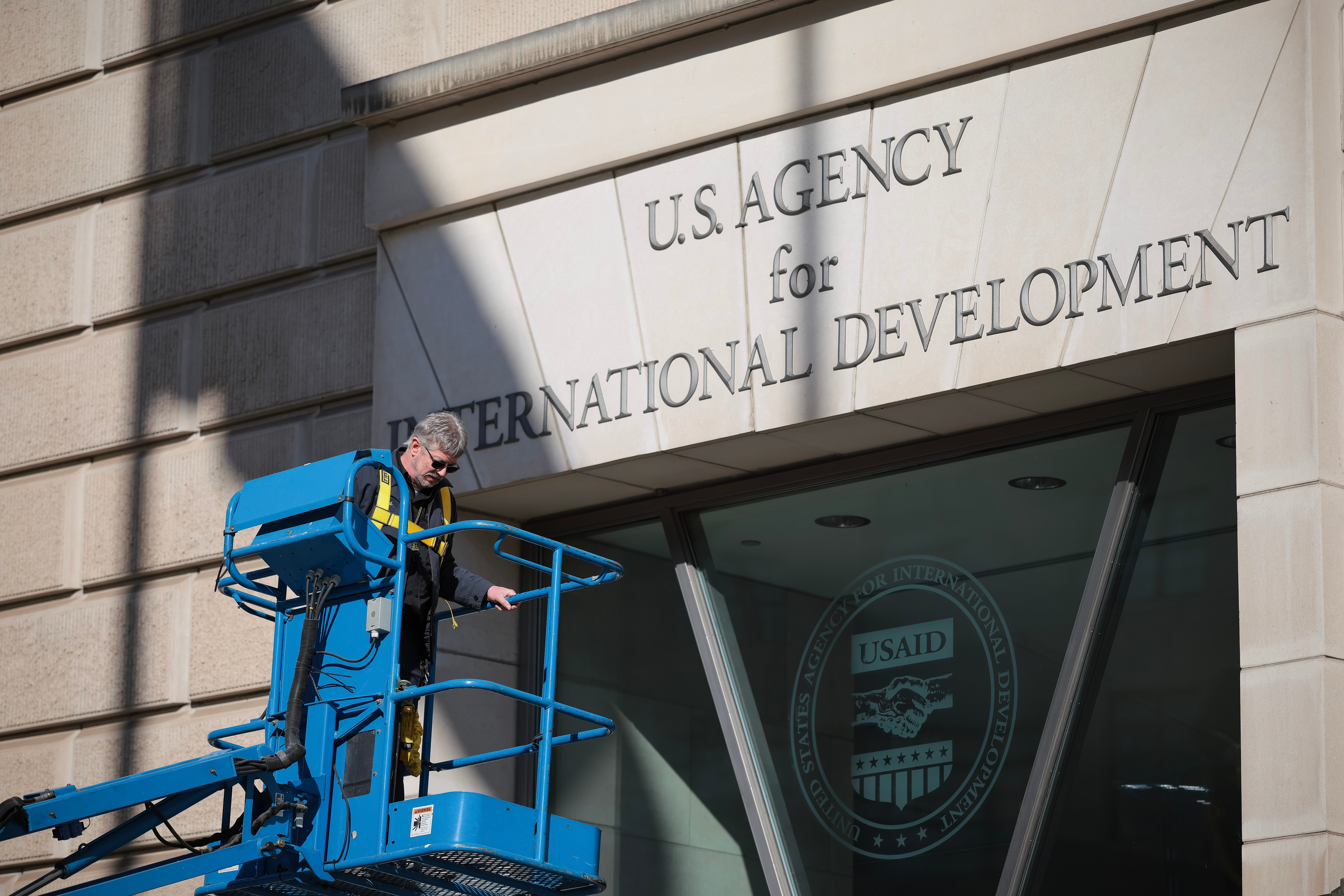 <p>A worker removes the U.S. Agency for International Development sign on their headquarters on February 07, 2025 in Washington, DC</p>