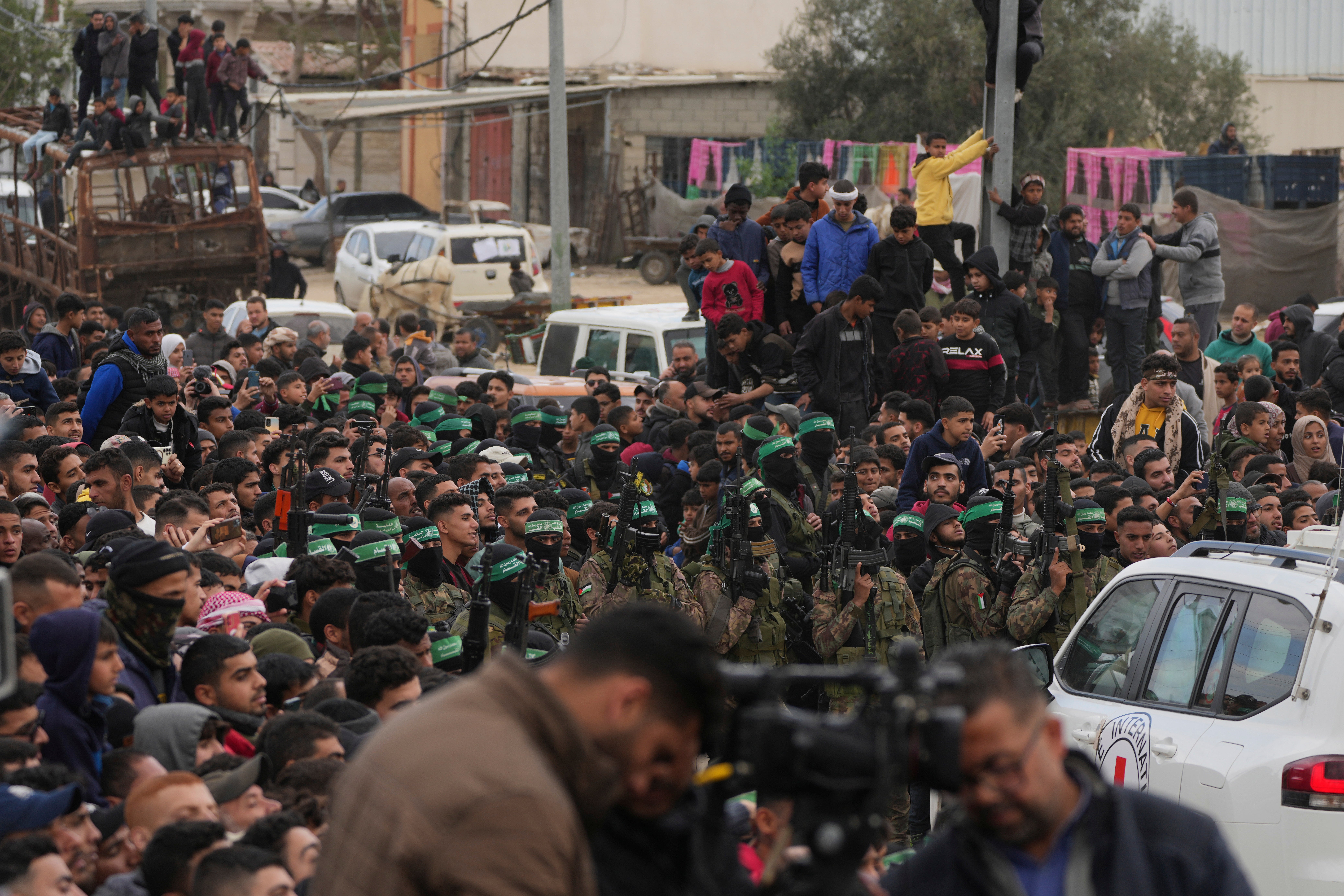 Palestinians gather as Hamas fighters escort Red Cross vehicles carrying Israeli captives Ohad Ben Ami, Eli Sharabi, and Or Levy