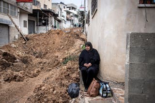 A woman sits on the side of a destroyed street while she waits for her to return to her home at Alphara's camp