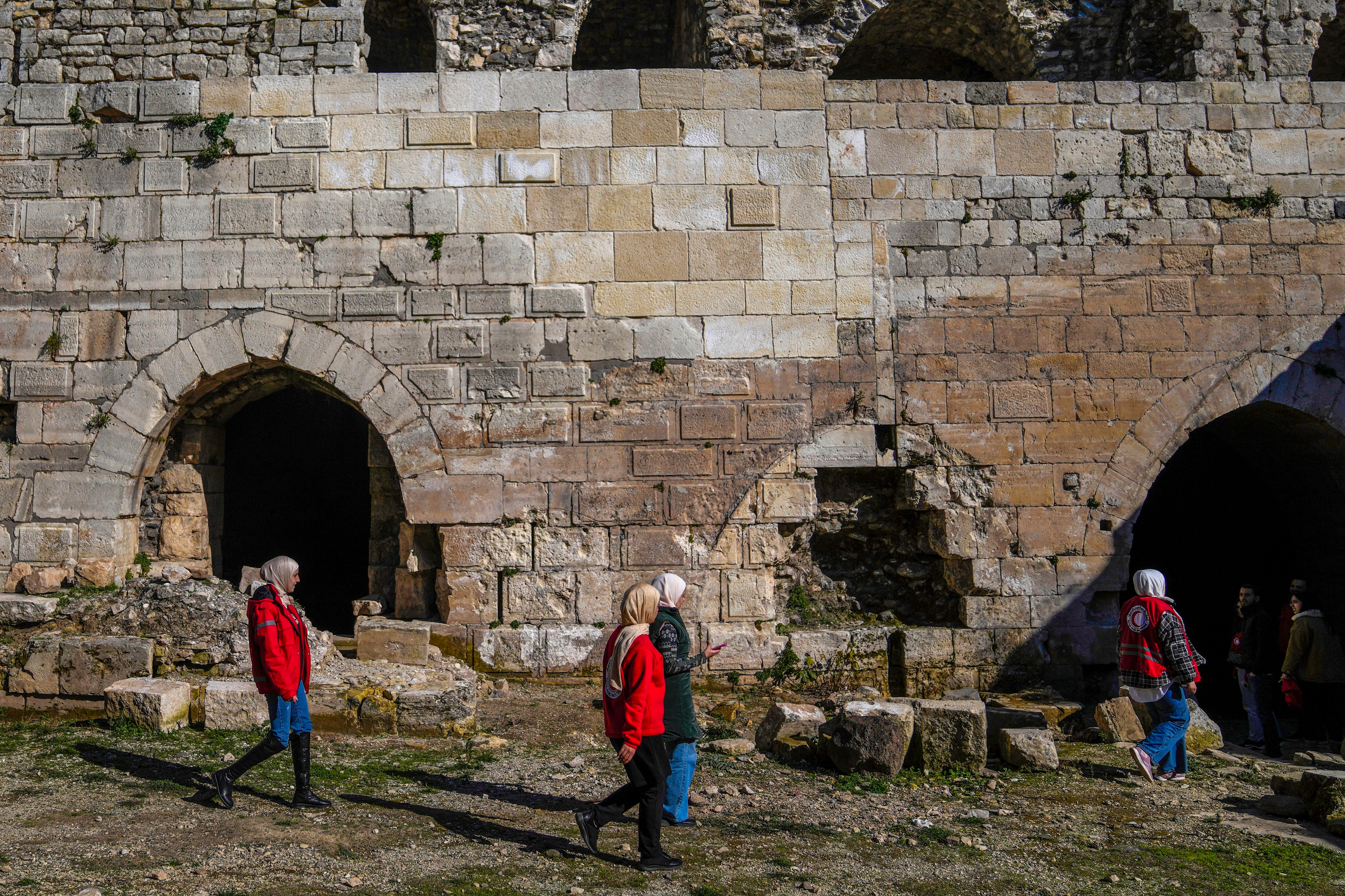 People walk past a damaged section of Krak des Chevaliers, whcih caused by the Assad regime shilling in 2014