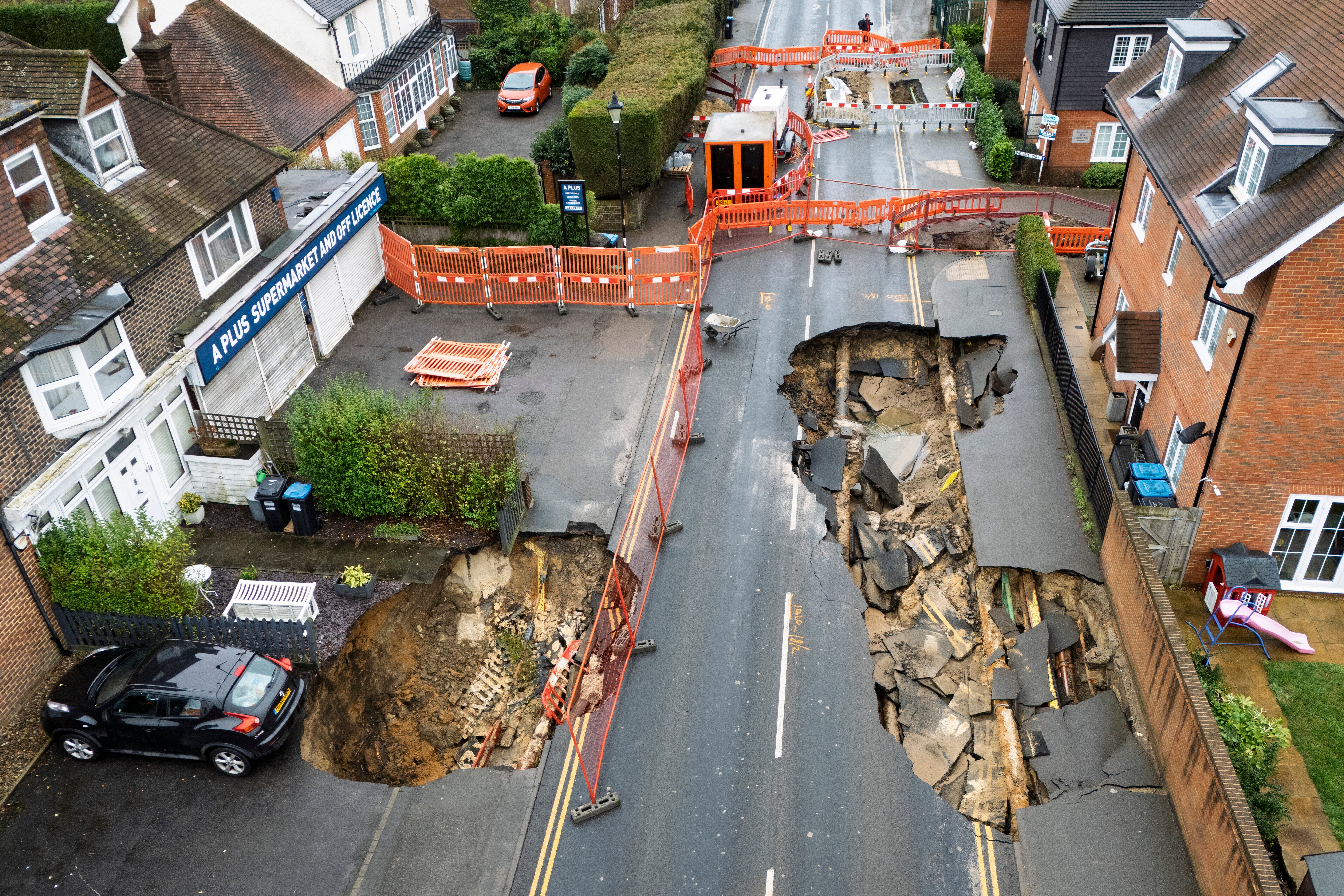 A black car is left teetering over the sinkhole