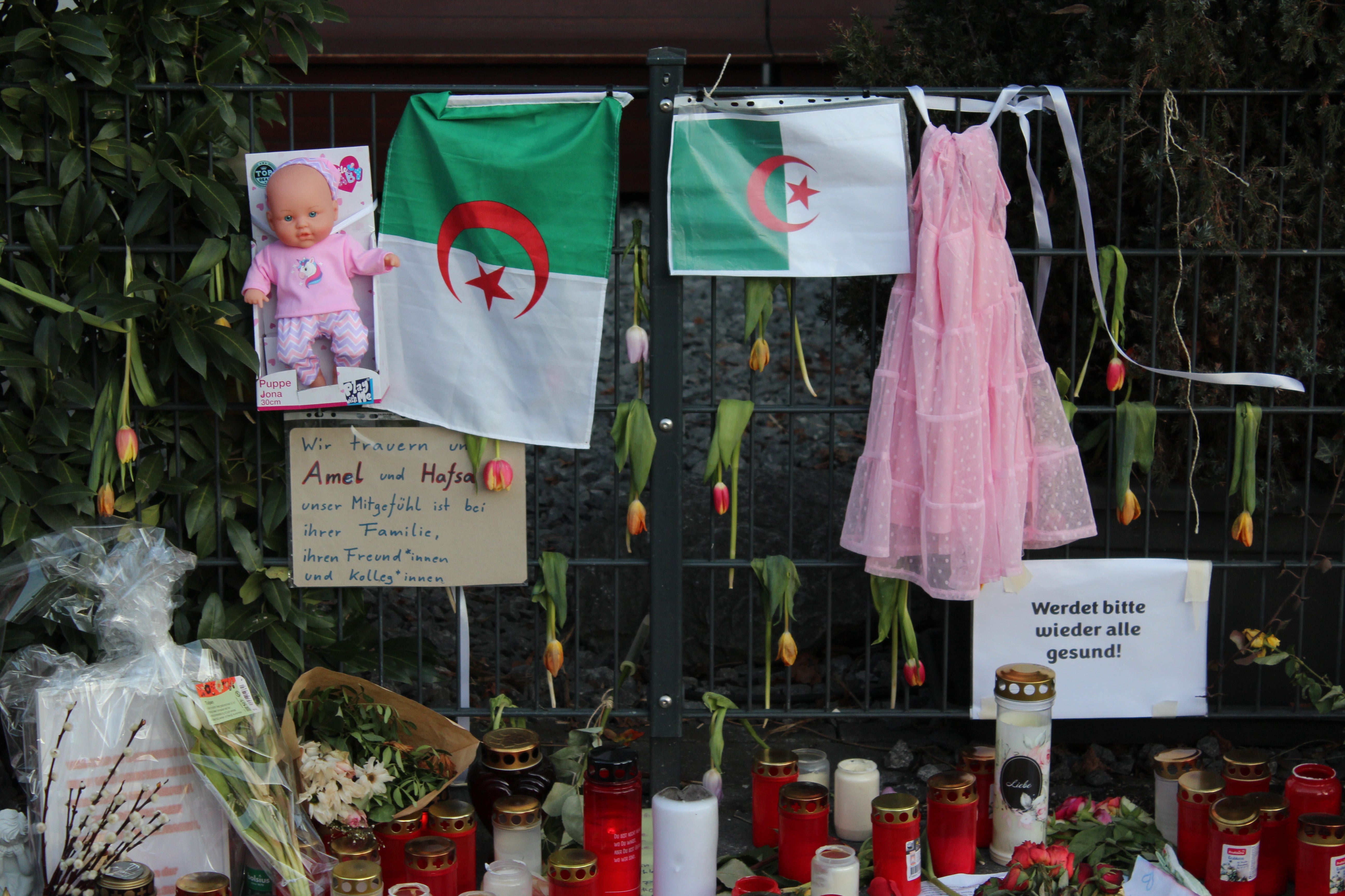 A pink dress and a baby doll are hung on either side of Algerian flags at a tribute in Munich by the scene of the attack