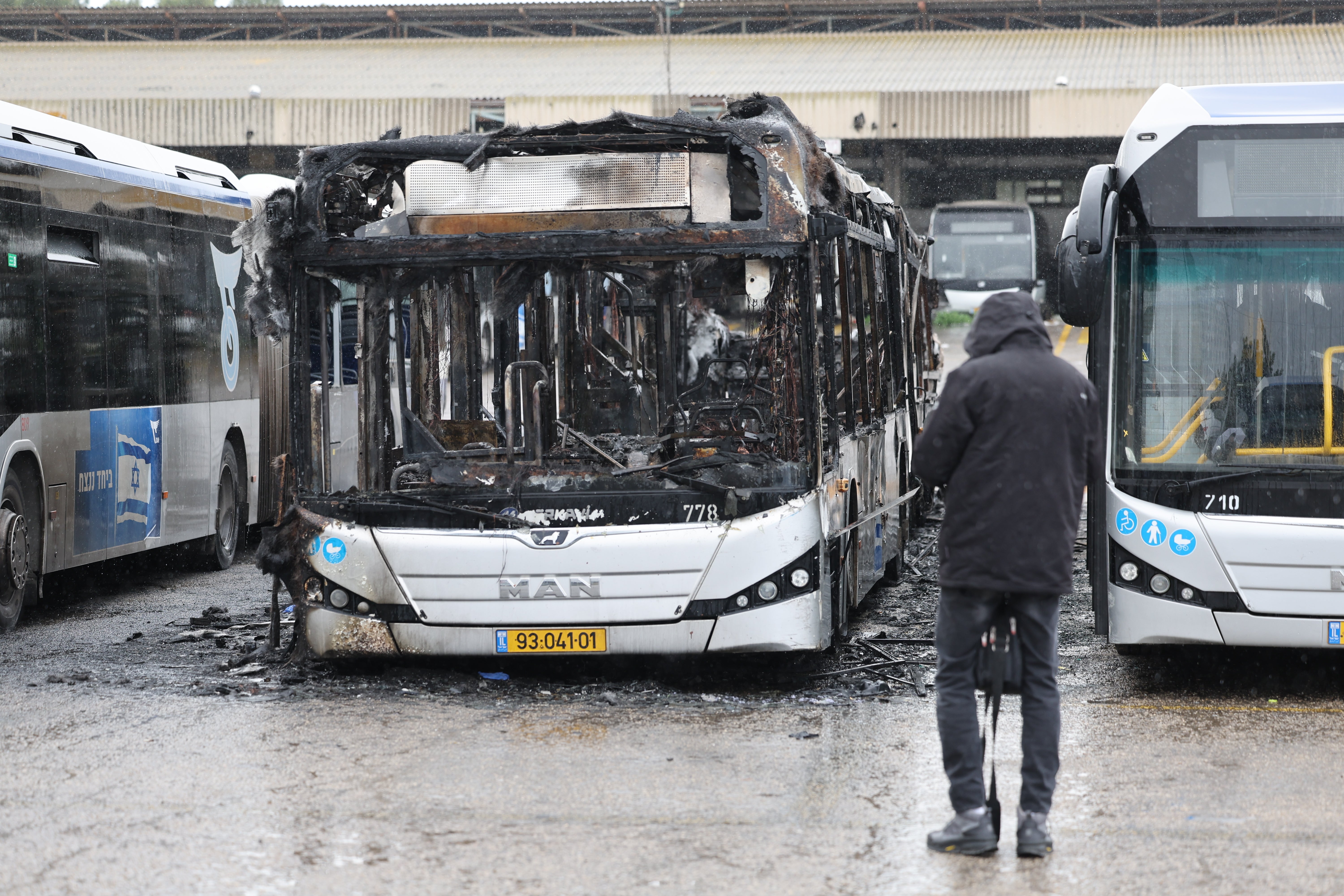 A person walks past a charred bus at the main bus parking lot following the explosions