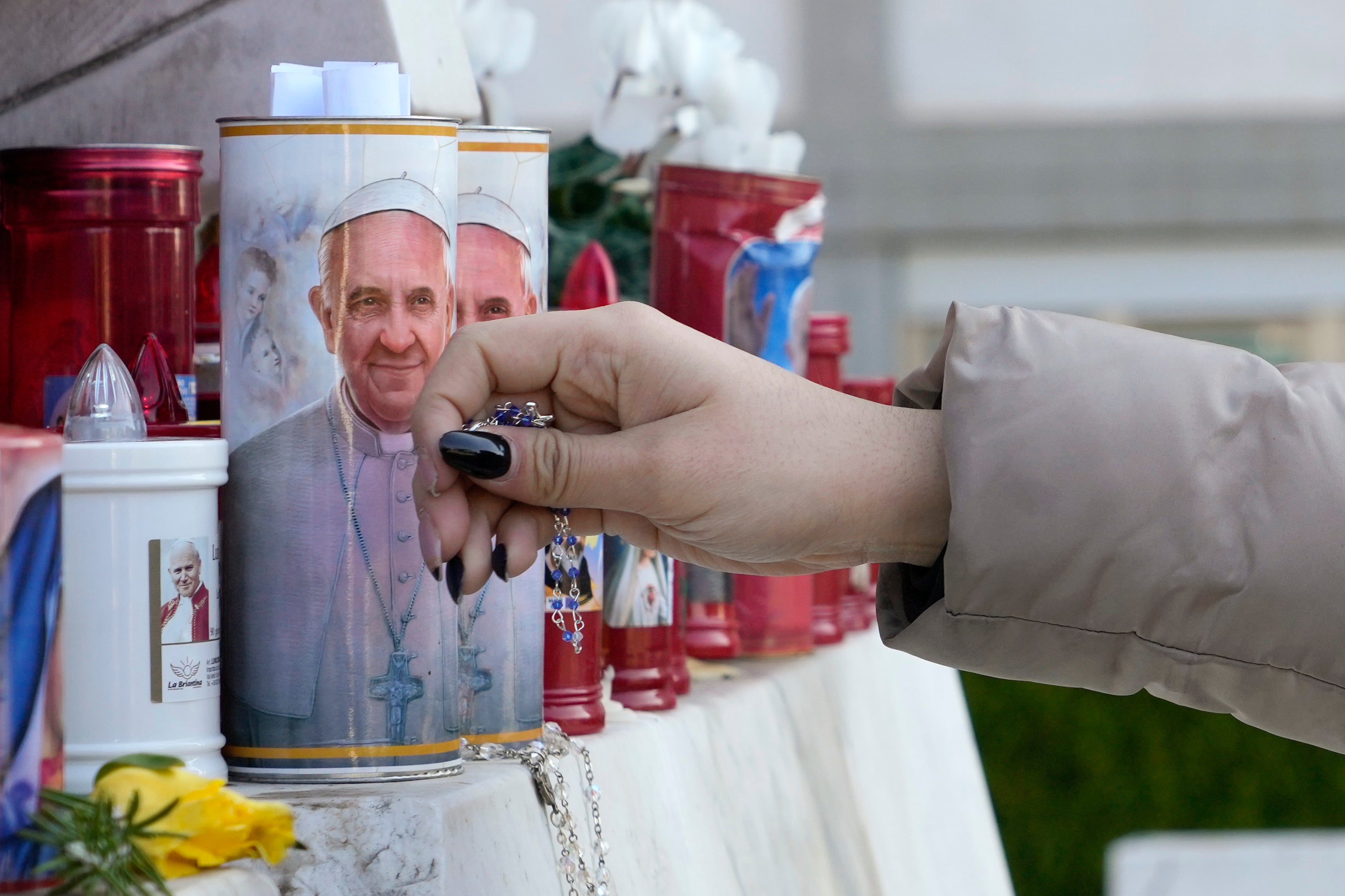 A woman lays a rosary near candles adorned with pictures of Pope Francis outside the Agostino Gemelli Polyclinic where Pope Francis is battling pneumonia, in Rome, Saturday, Feb. 22, 2025