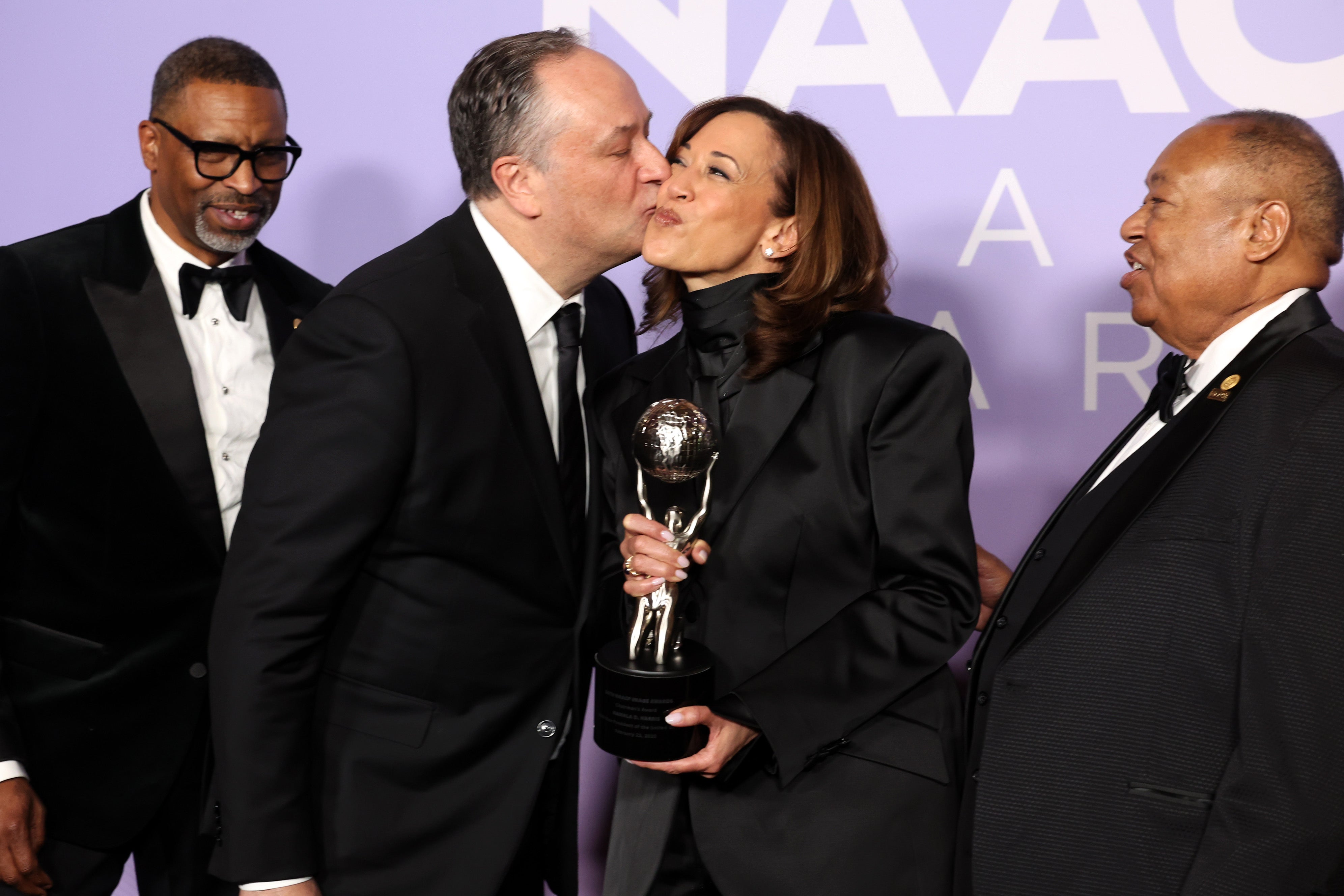 Kamala Harris holds the Chairman's Award while her husband, Doug Emhoff, kisses her cheek