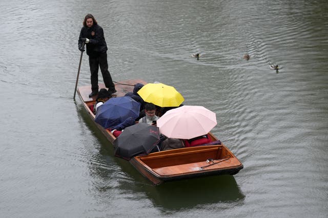 People shelter from the rain under umbrellas as they punt along the River Cam in Cambridge (Joe Giddens / PA).