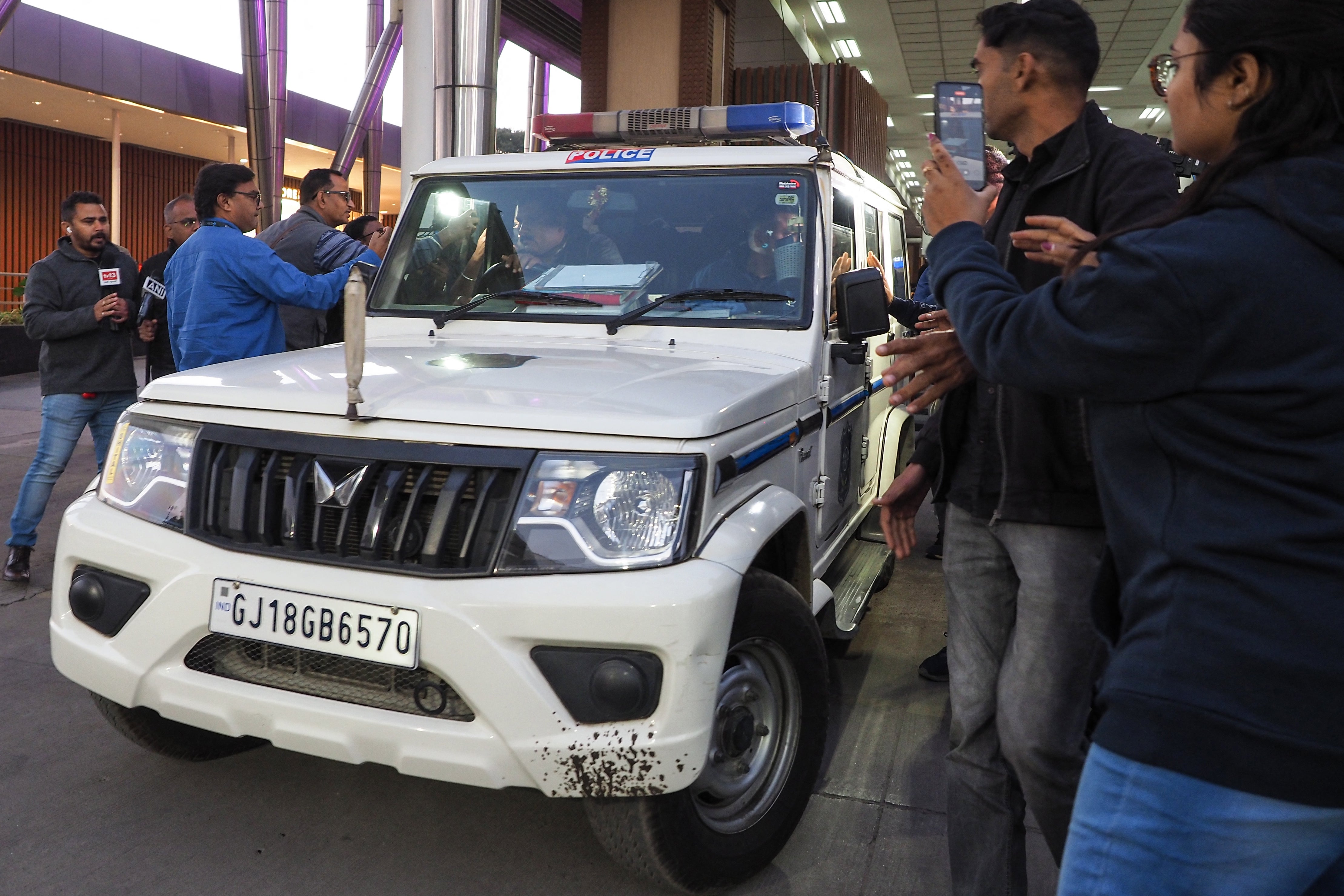 <p>Reporters gather around a police car transporting Indian migrants deported from the US at the Ahmedabad airport on 6 February 2025</p>