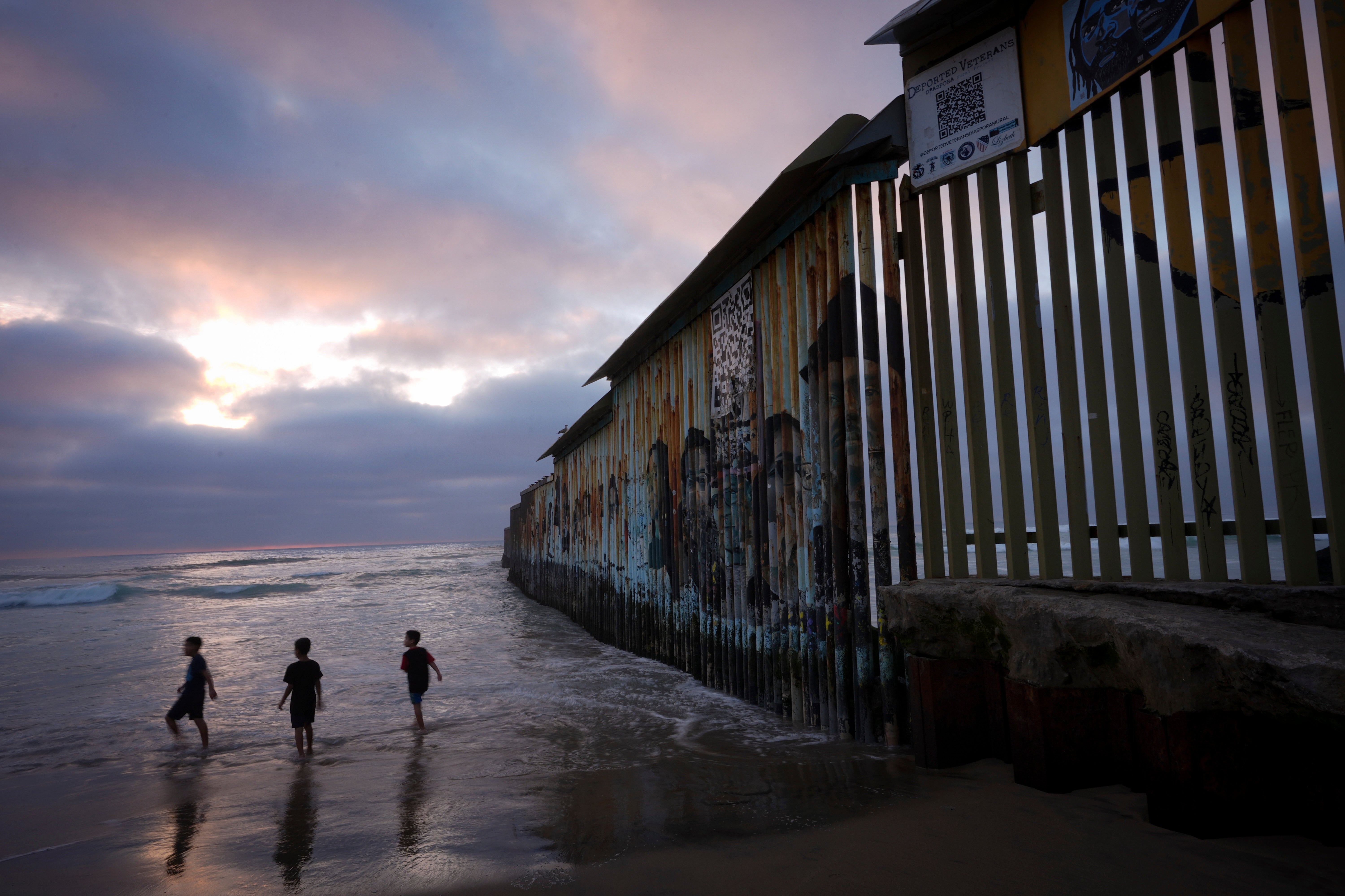 Three children play where the border wall between the US and Mexico meets the Pacific Ocean