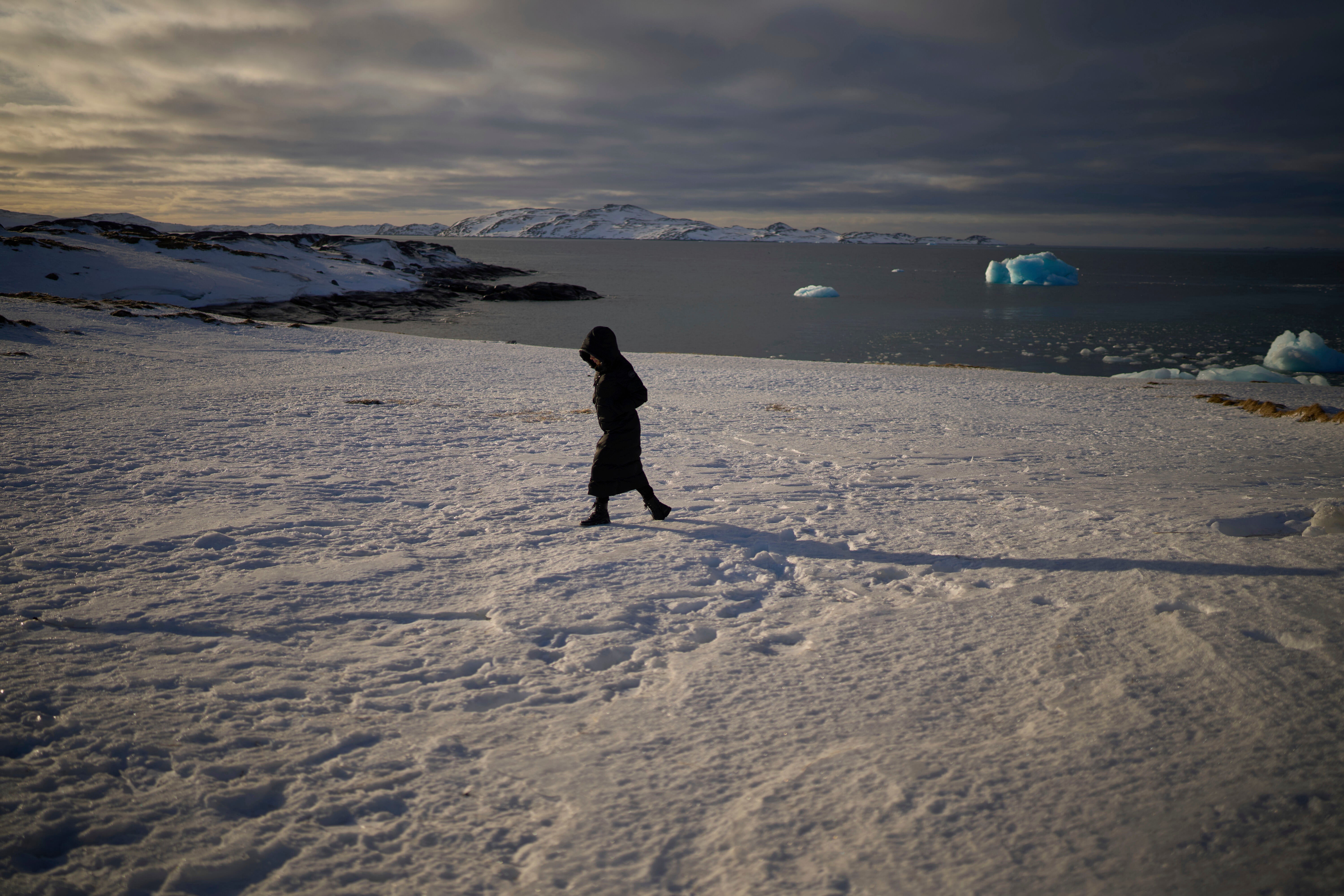 A woman walks along the shore of a beach in Nuuk, Greenland