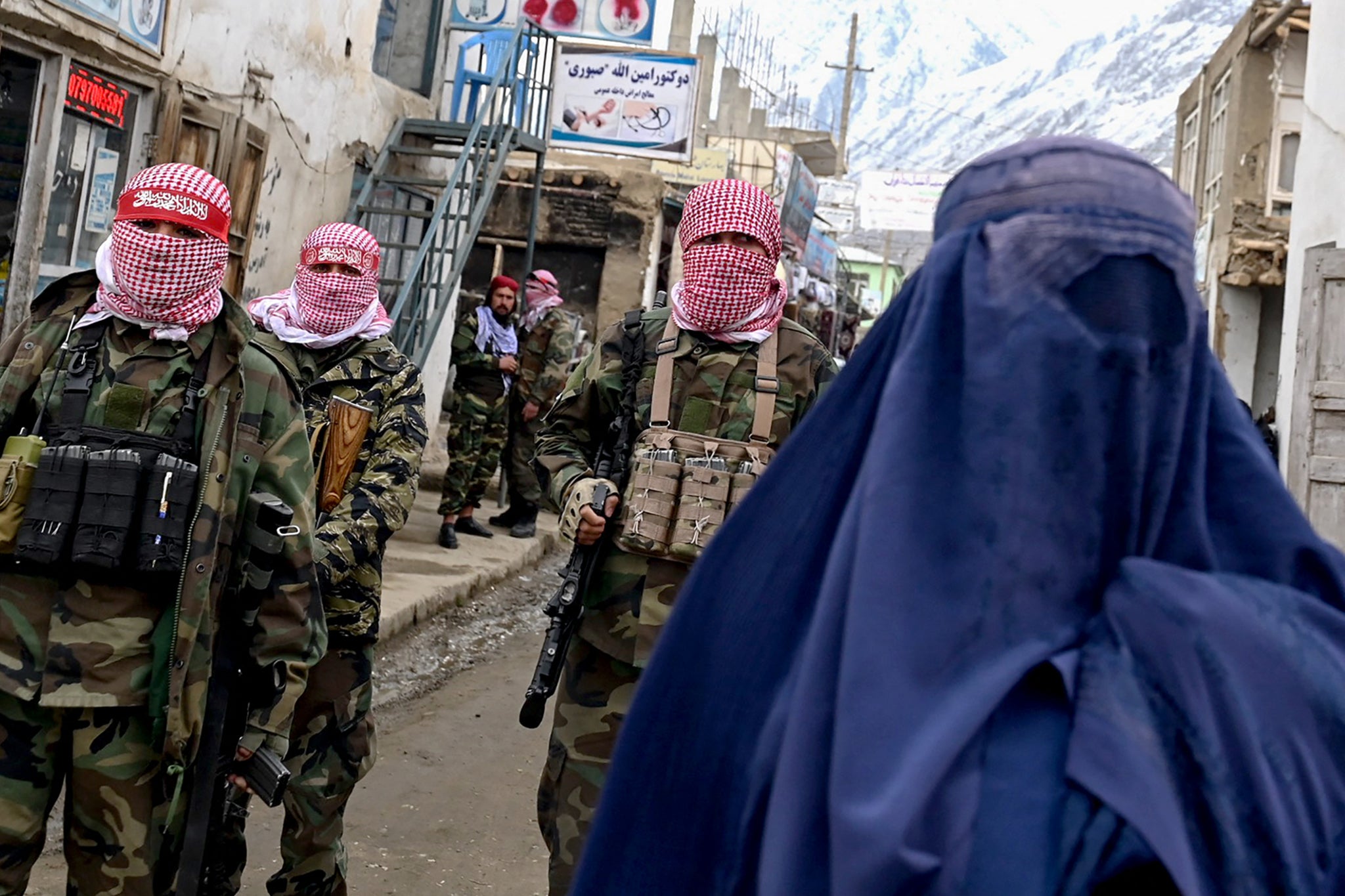 Taliban security personnel stand guard as an Afghan burqa-clad woman (R) walks along a street at a market in the Baharak district of Badakhshan province on 26 February 2024